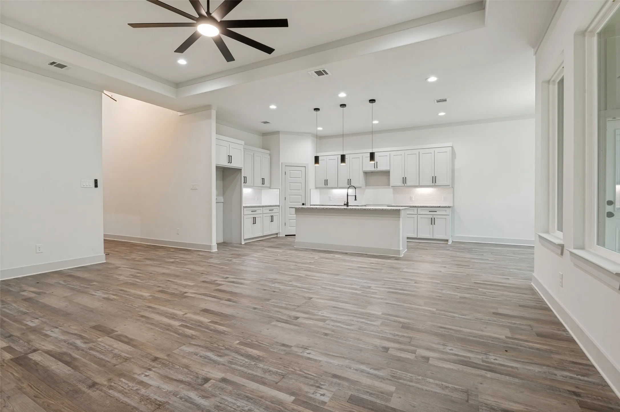 Open-concept living space featuring wood-finish flooring, a contemporary ceiling fan, recessed lighting, and white cabinetry