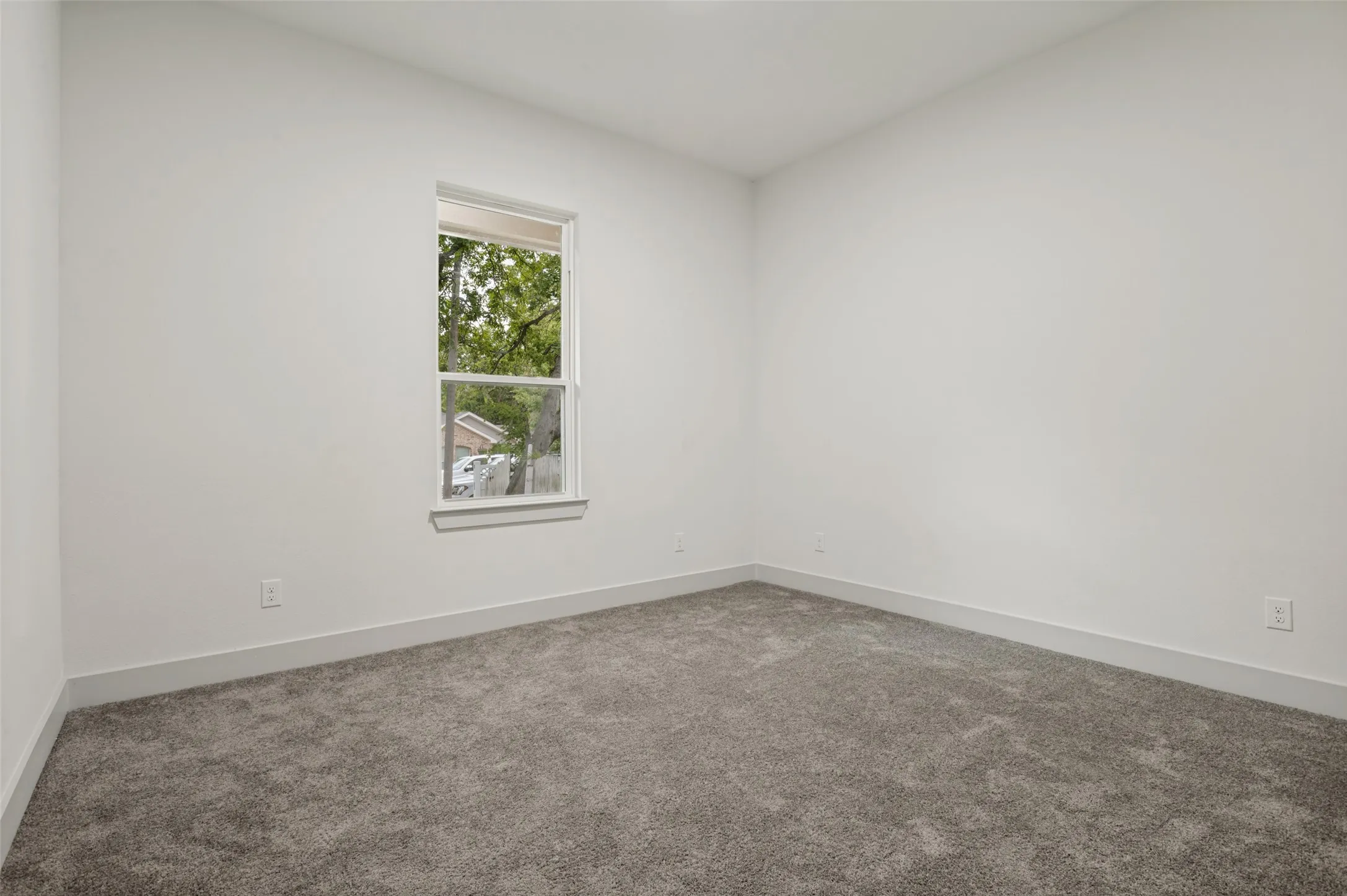 Bright, light-filled bedroom featuring a large double-hung window with natural light, neutral wall finishes, and neutral-toned carpet flooring