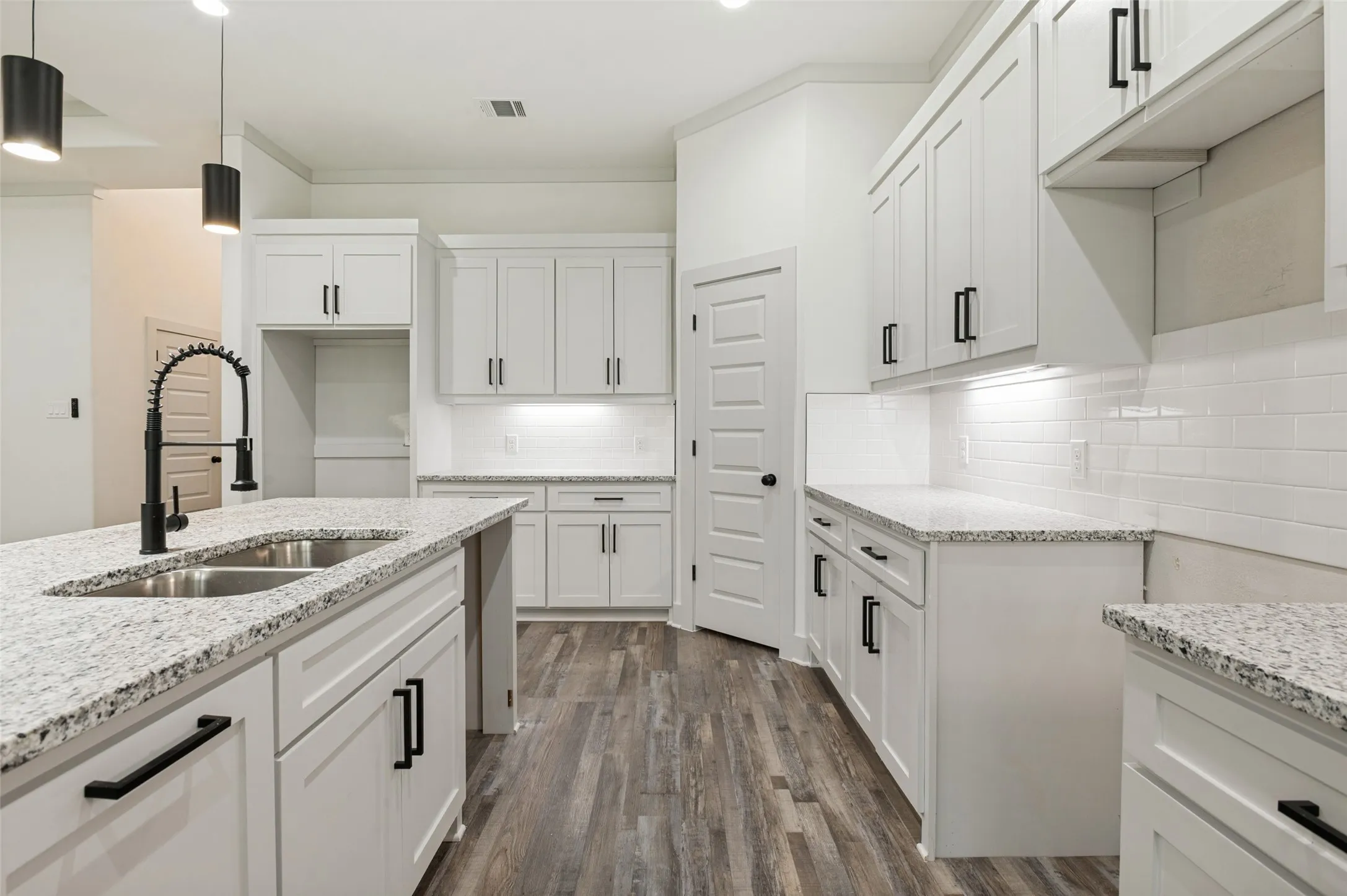 Modern kitchen featuring white shaker-style cabinetry, granite countertops, stainless steel appliances, a gooseneck faucet with pulldown spray, and wood-finish flooring throughout the open layout