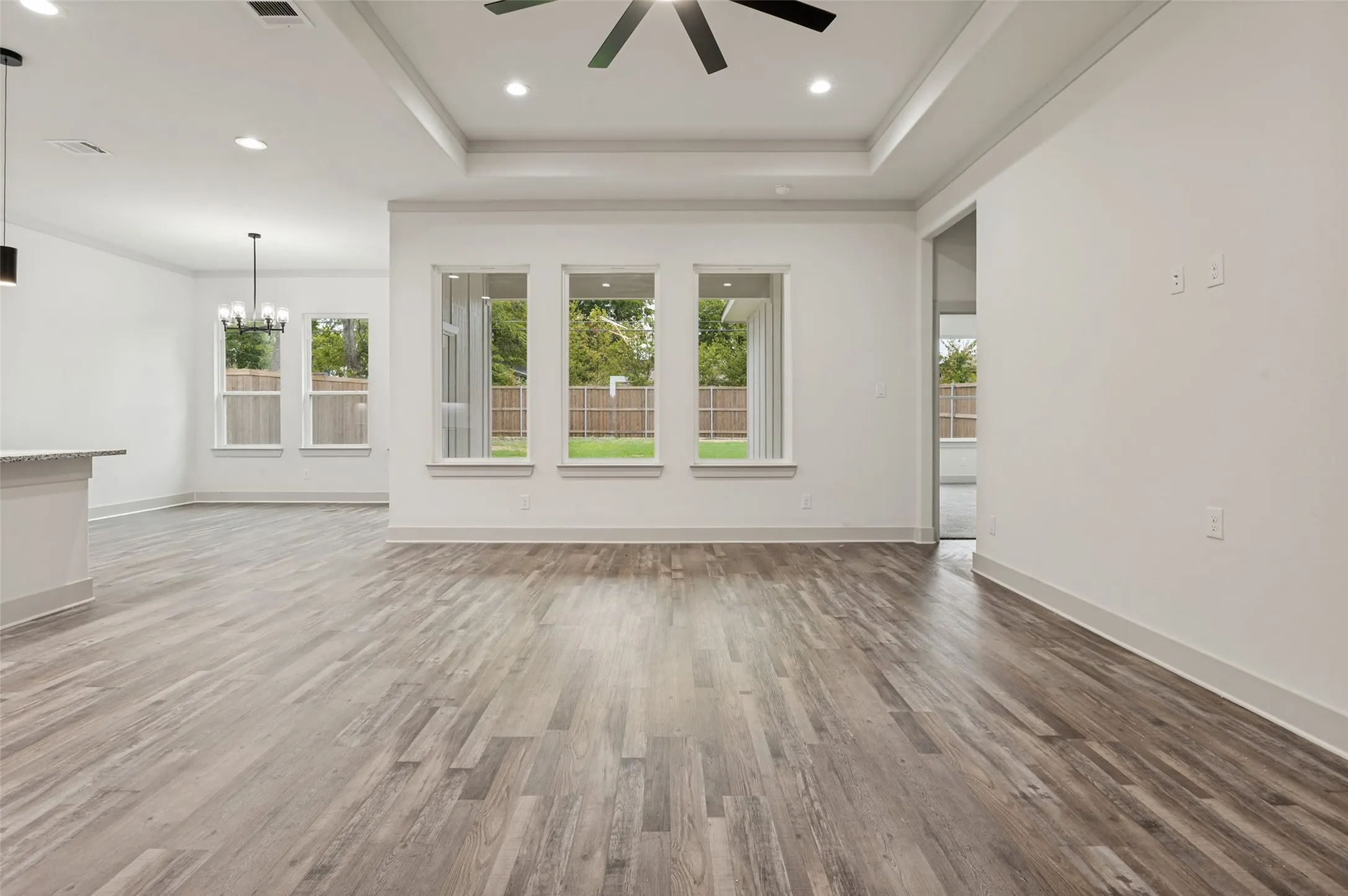 Wood-finish flooring throughout, recessed lighting, tray ceiling, multiple windows, and a ceiling fan