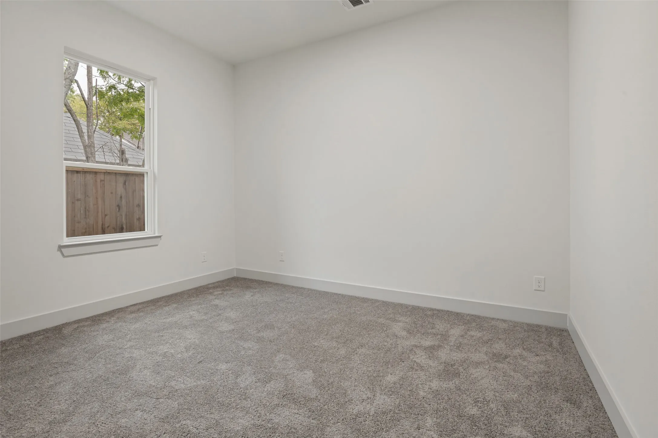 White walls with a single window, gray carpeting, and white trim