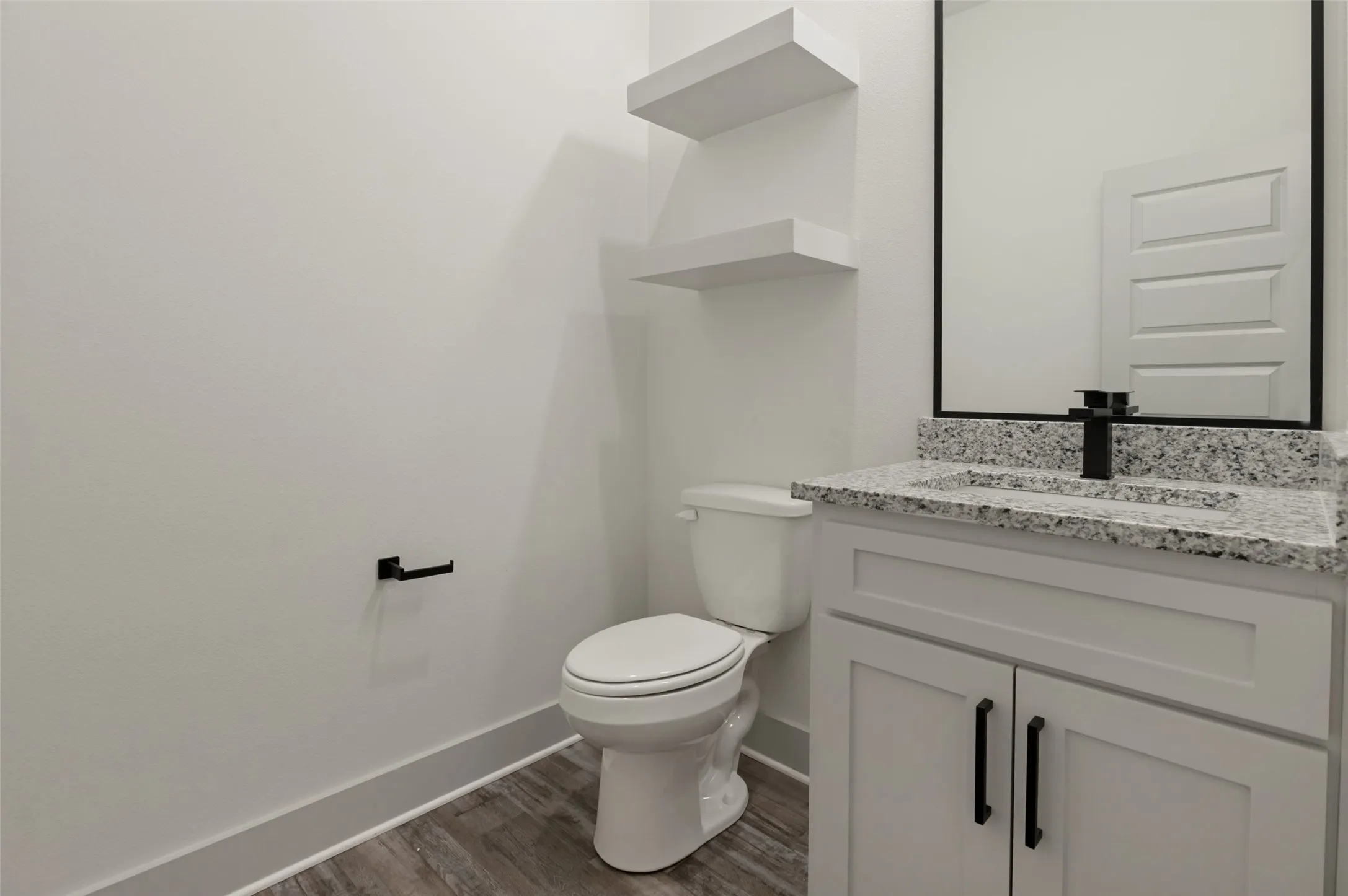 Modern bathroom featuring a sleek vanity with dual black hardware pulls, speckled quartz countertop, and a framed mirror above