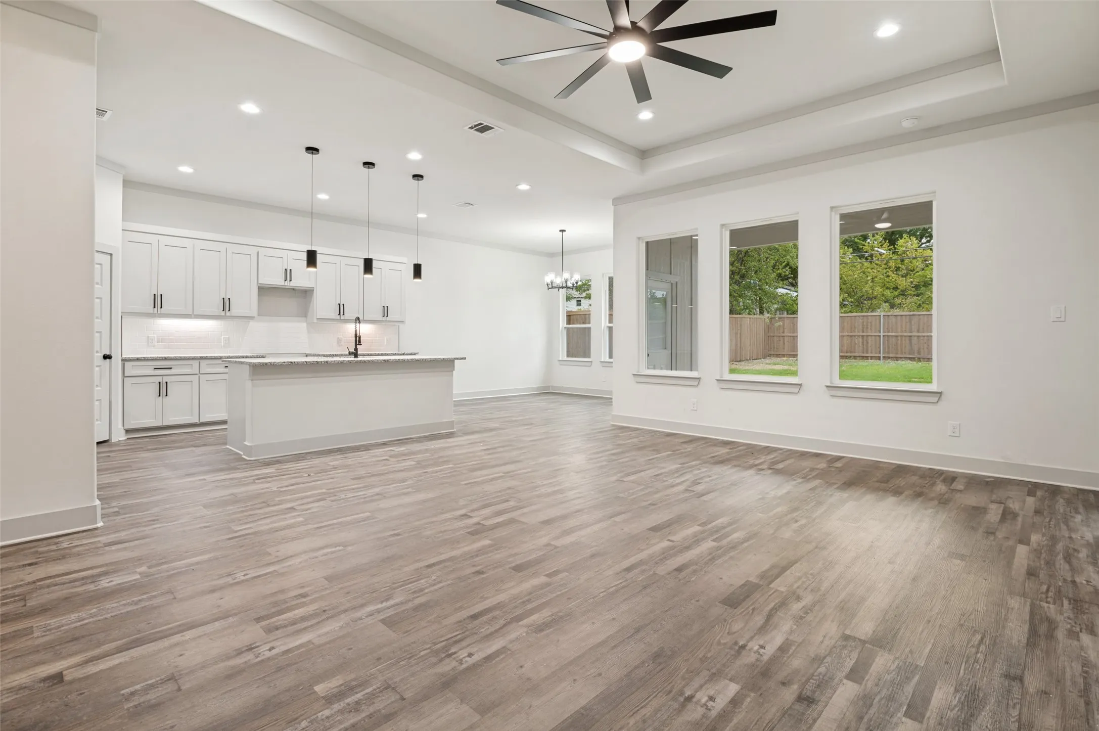 Wood-finish flooring throughout, tray ceiling with a ceiling fan, recessed lighting, and multiple windows