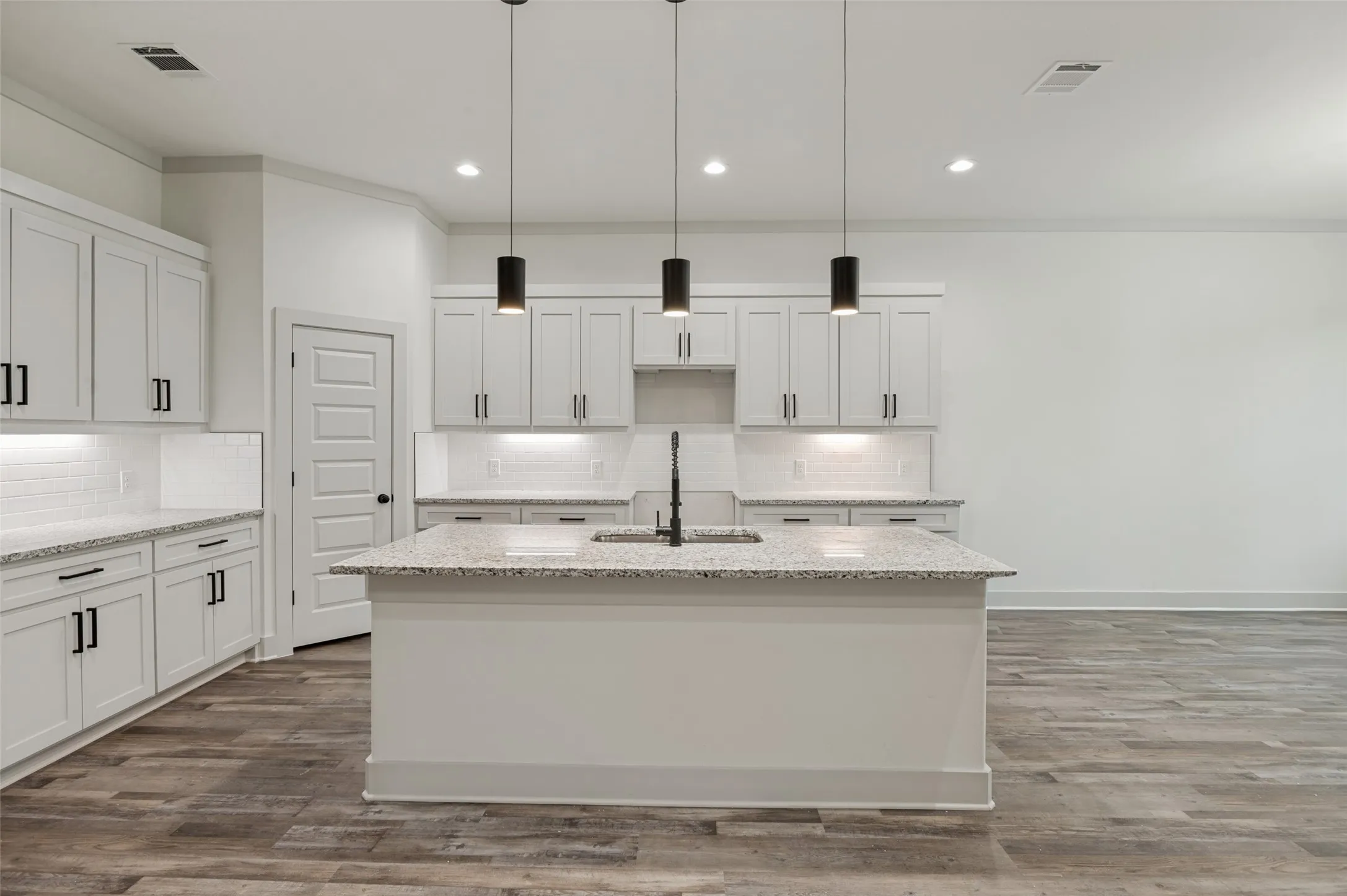 Kitchen featuring white cabinetry, granite countertops, a subway tile backsplash, a center island with sink, and wood-finish flooring