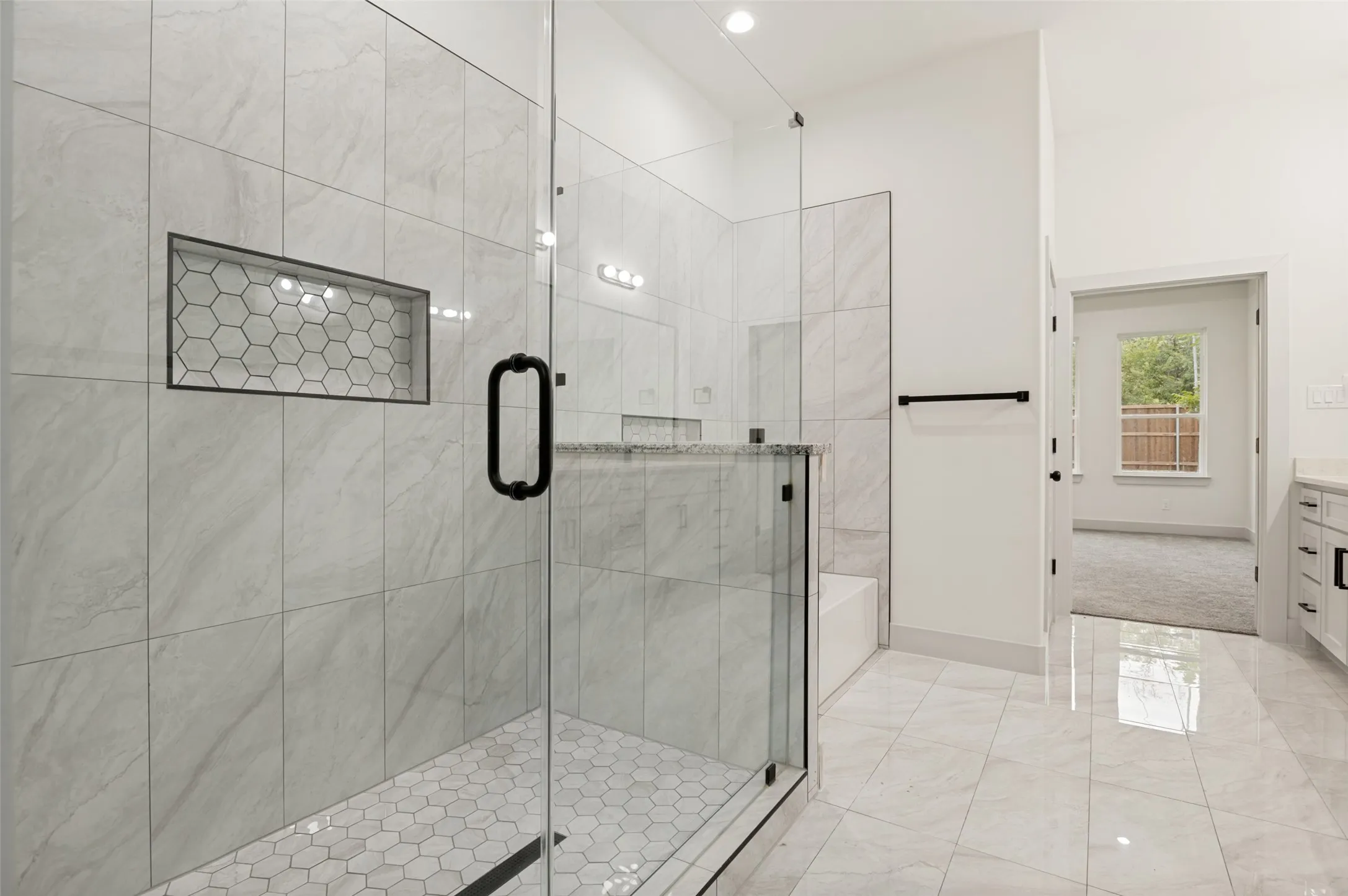Glass-enclosed shower with a hexagonal tile floor, recessed tile niche, and matte black fixtures