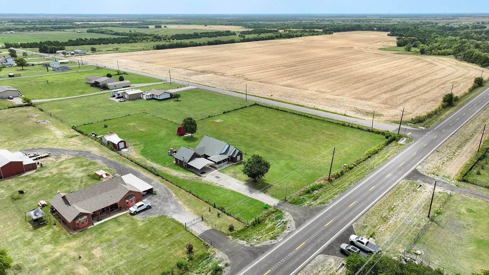 Expansive rural property featuring a main residence with a covered porch, an additional structure, and a red barn on a large lot with mature trees