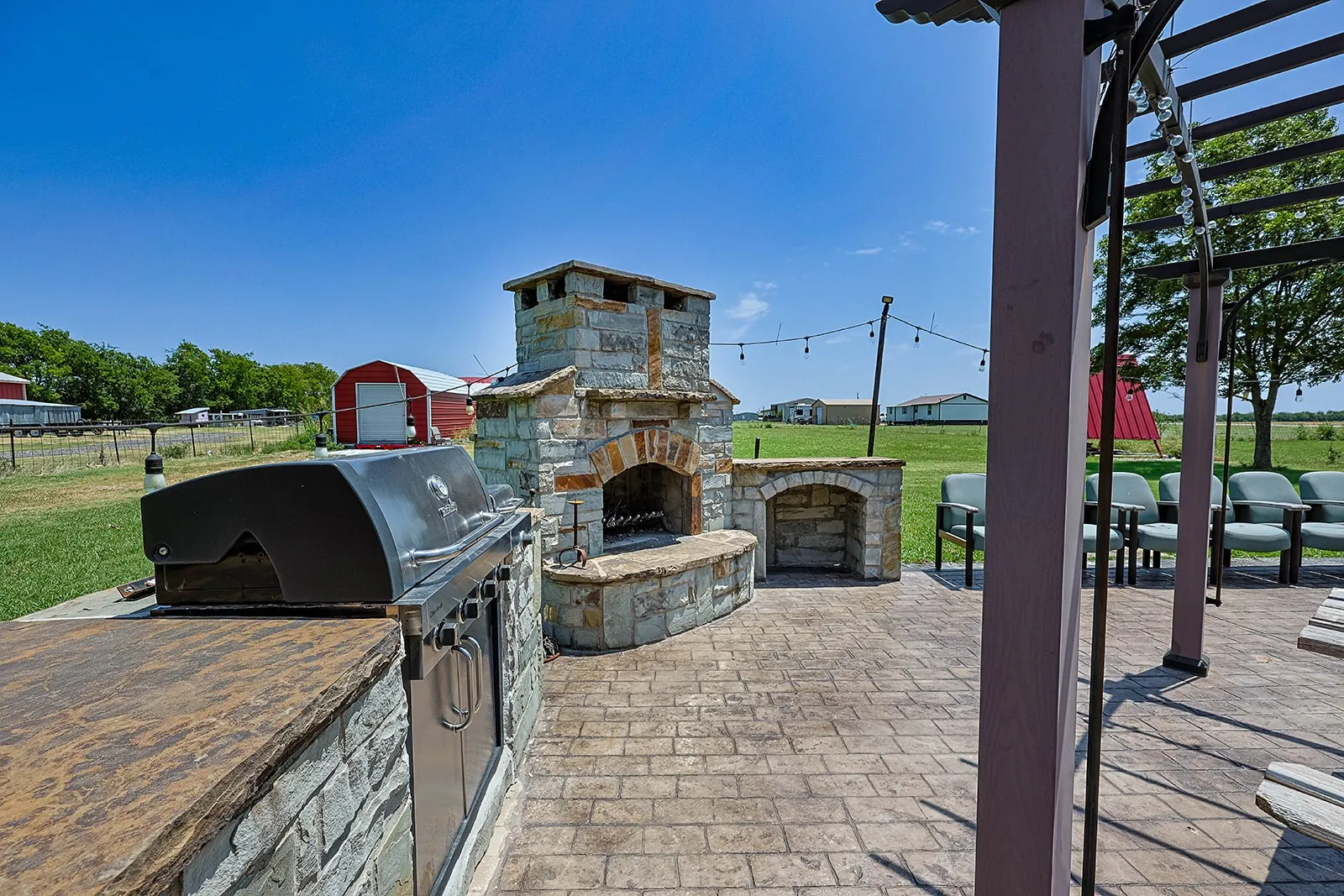 Outdoor kitchen featuring a built-in grill, stone-faced cabinetry, and a stone-clad fireplace