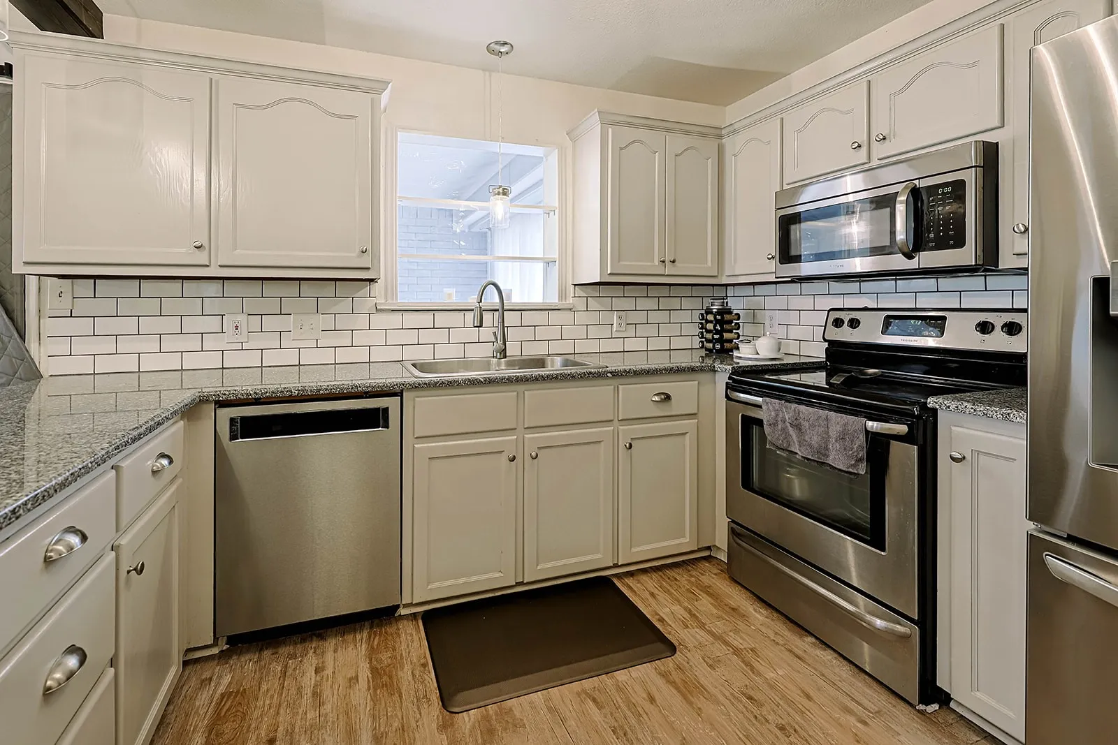 Kitchen featuring light-toned cabinetry, stainless steel appliances, granite countertops, subway tile backsplash, and wood-finish flooring