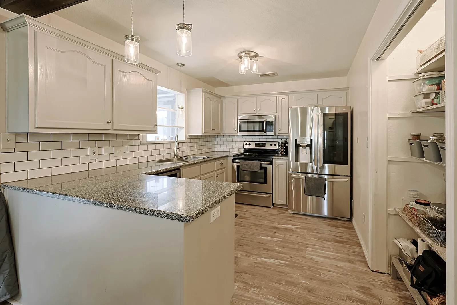 Kitchen featuring granite countertops, subway tile backsplash, stainless steel appliances, wood-finish flooring, and pantry with built-in shelving
