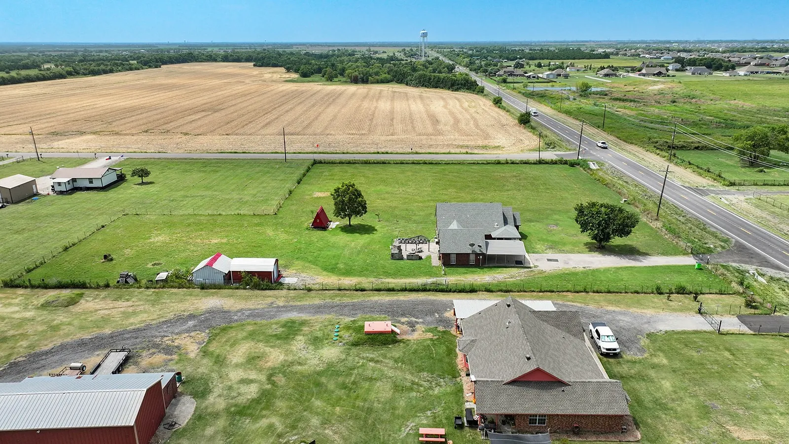 Expansive property featuring a brick residence with a dark shingle roof, a secondary structure with a red roof, and a large open field