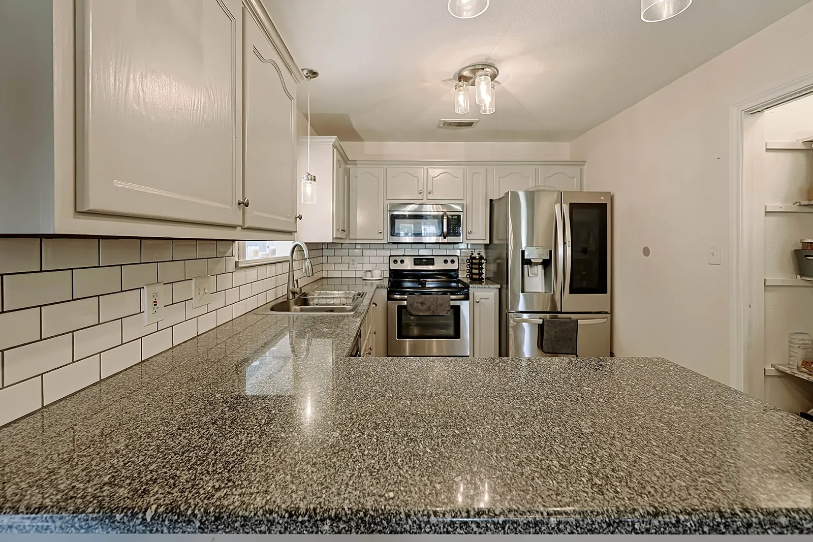 Kitchen featuring speckled countertops, white subway tile backsplash, white cabinetry, stainless steel appliances, and recessed shelving