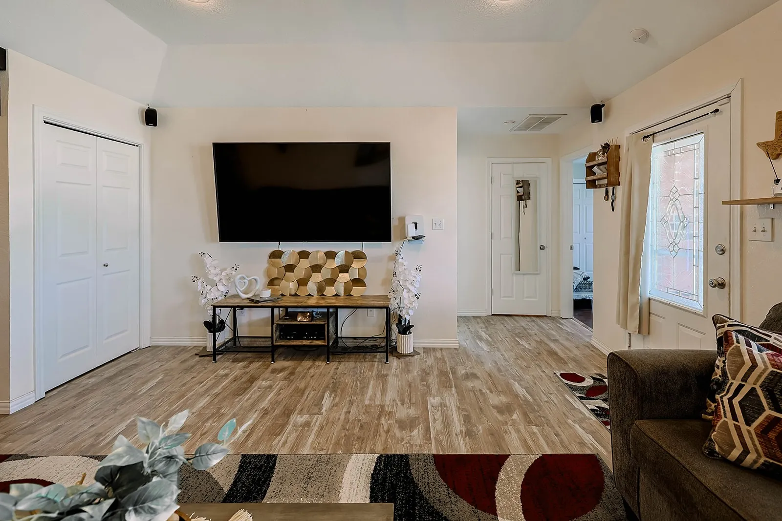 Spacious open-concept living area featuring wood-finish flooring, vaulted ceilings, and a paneled white door