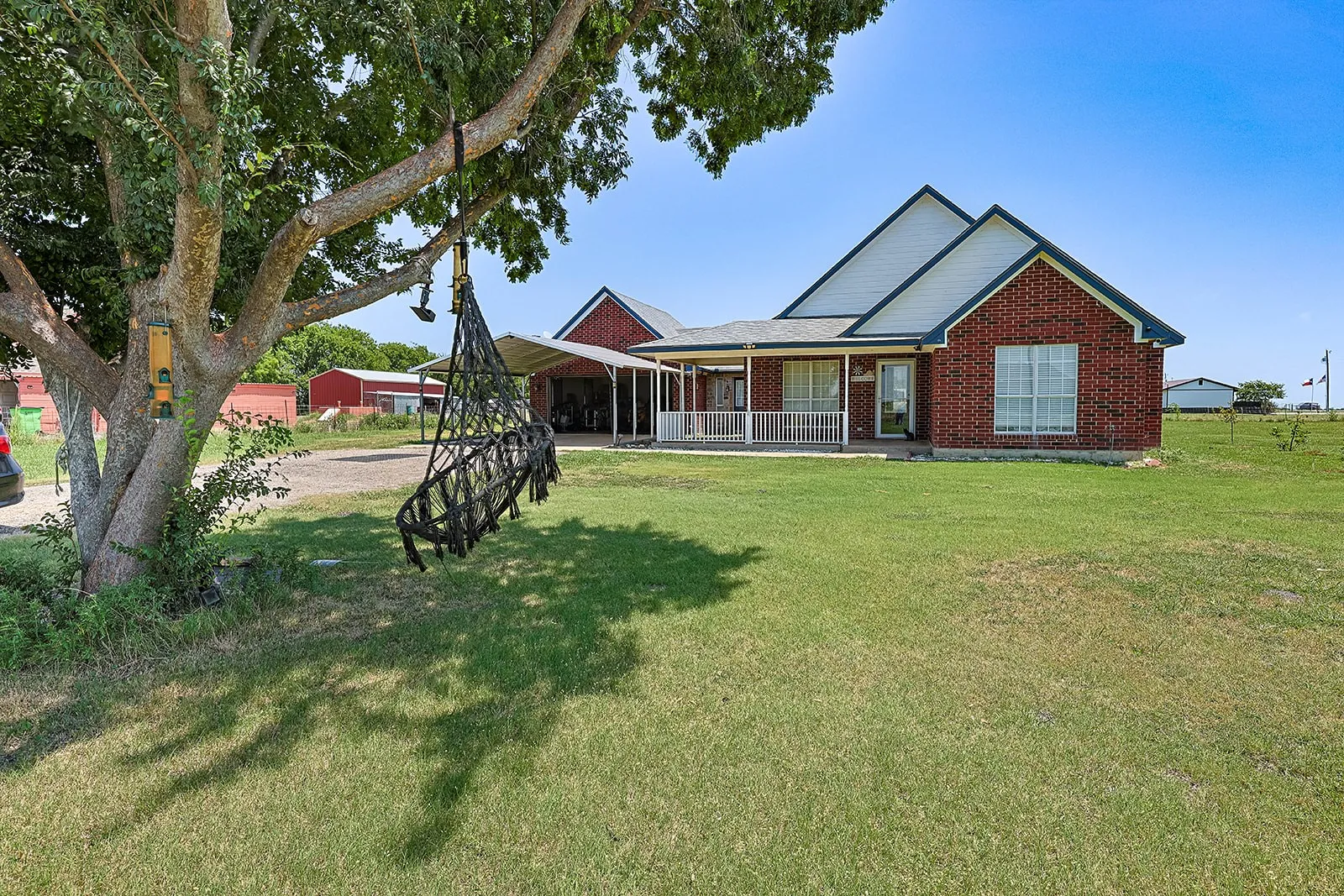 Brick-clad ranch home featuring a covered front porch with white railing, a double gable roofline, and an expansive lawn