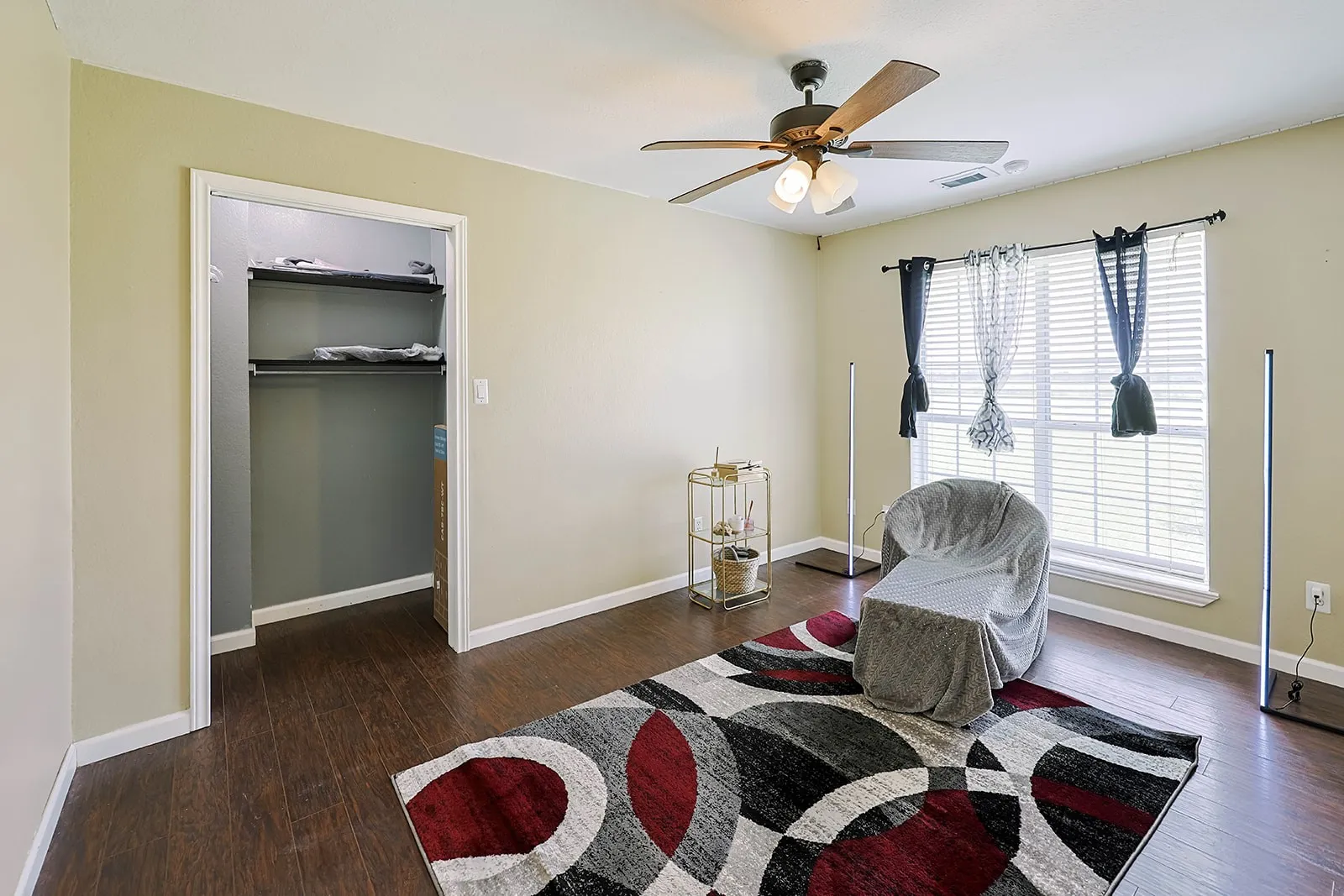 Spacious room featuring wood-finish flooring, a ceiling fan with integrated lighting, and a large window with blinds