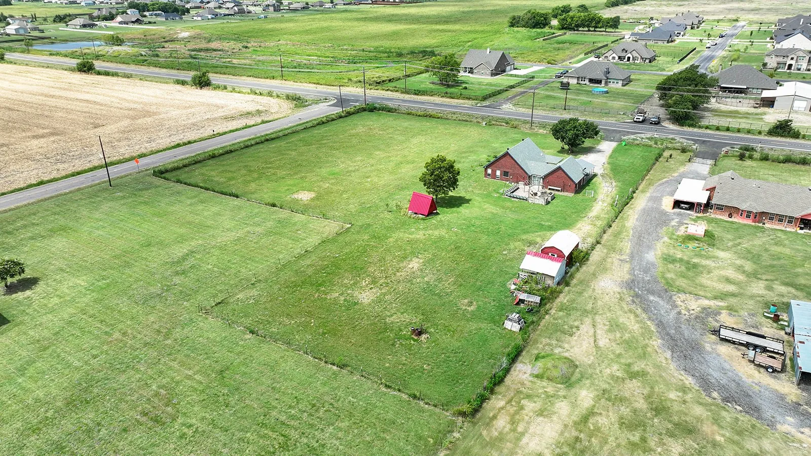 Expansive green acreage featuring a primary residence with a red roof, a red barn, and additional outbuildings
