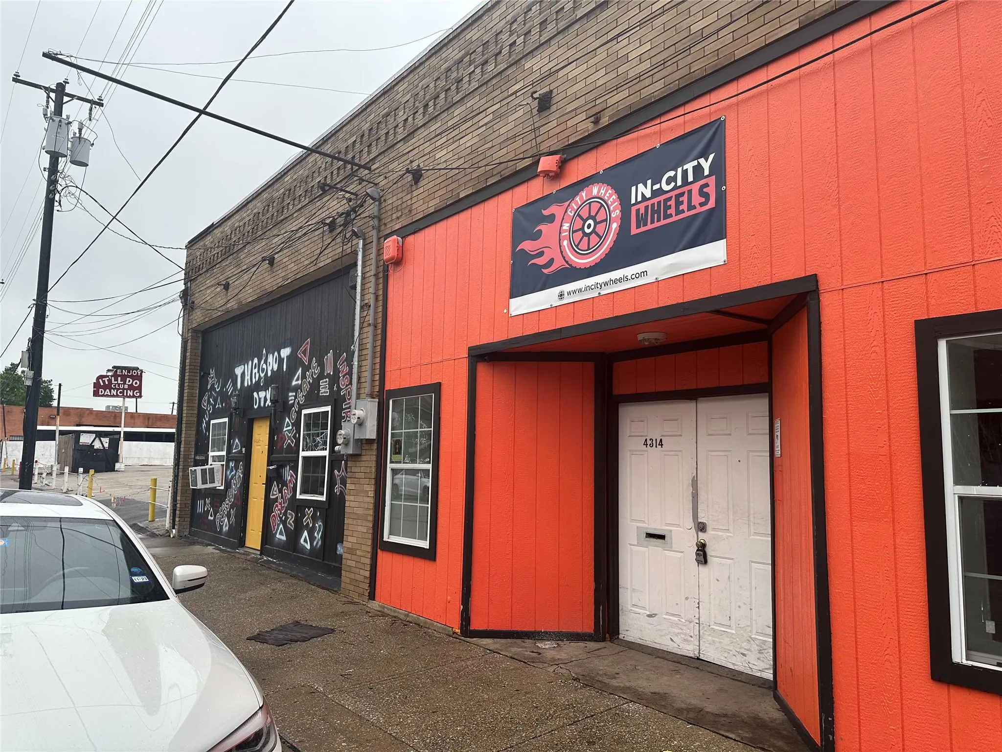 Commercial building featuring an orange facade with dark trim, a recessed entrance, and a secondary black facade with multiple windows