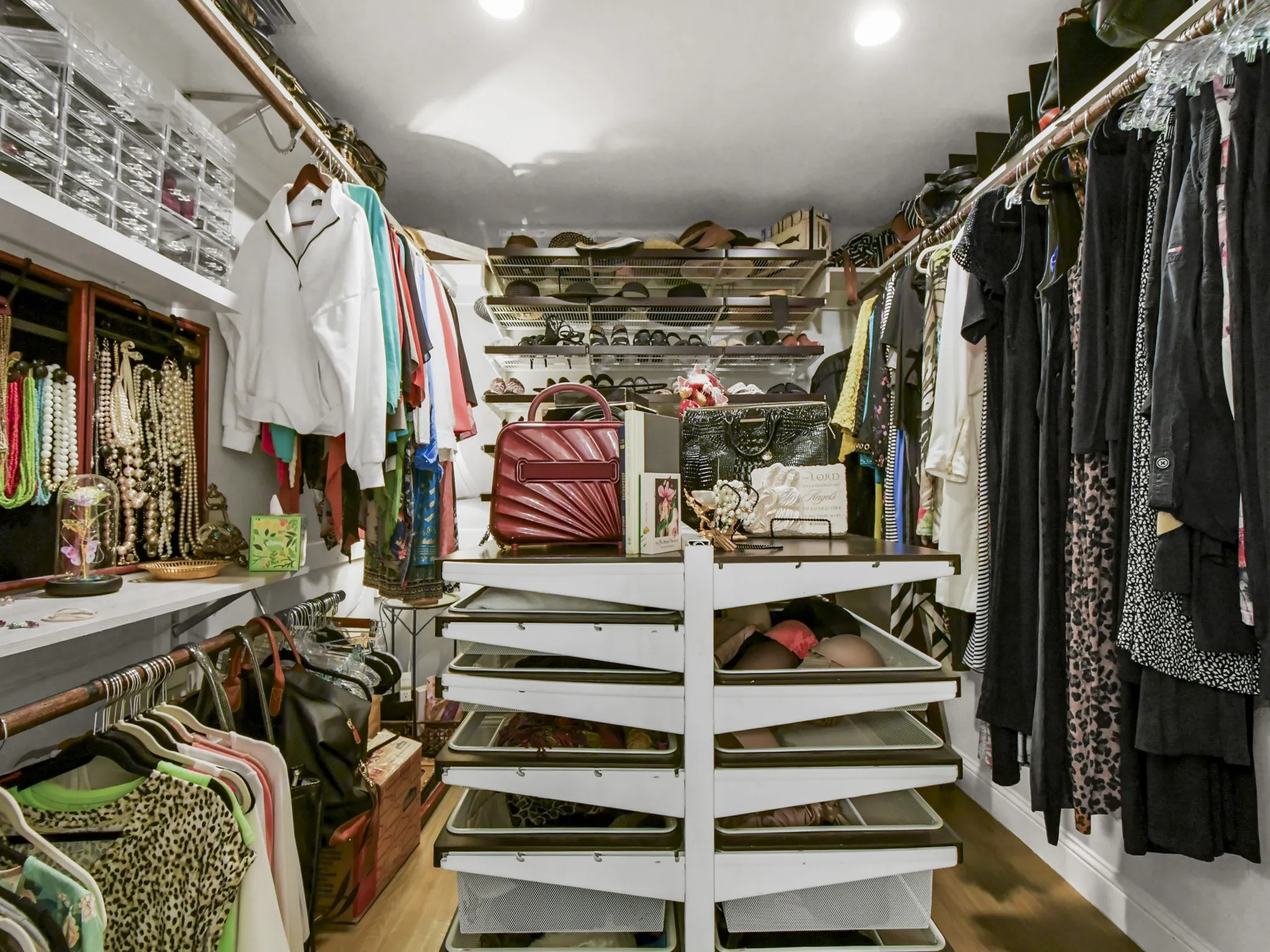 Custom closet organization system featuring multiple hanging rods, integrated shelving, and a central island with pull-out drawers