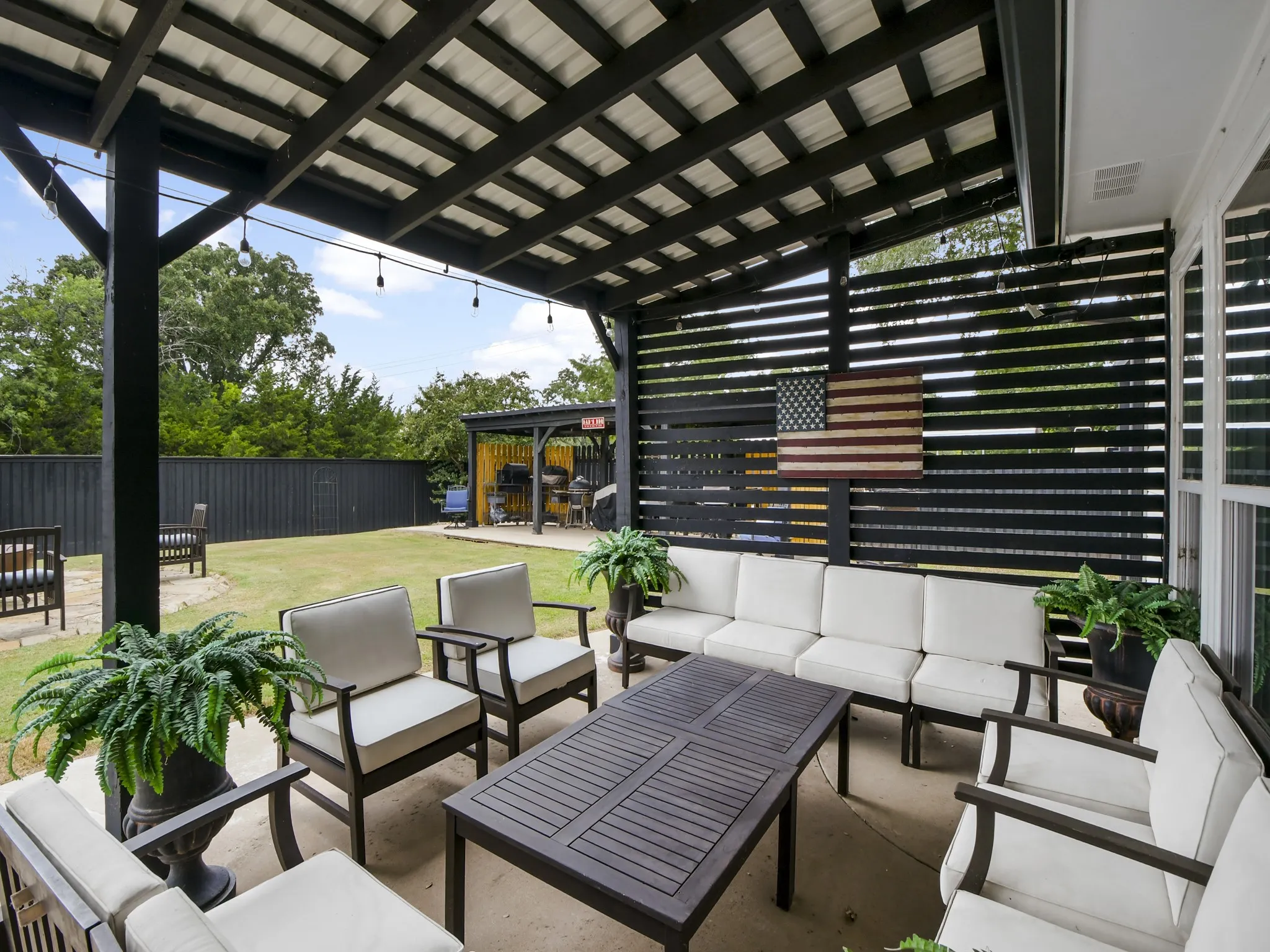 Covered patio featuring a slatted privacy wall, concrete flooring, and a corrugated metal roof