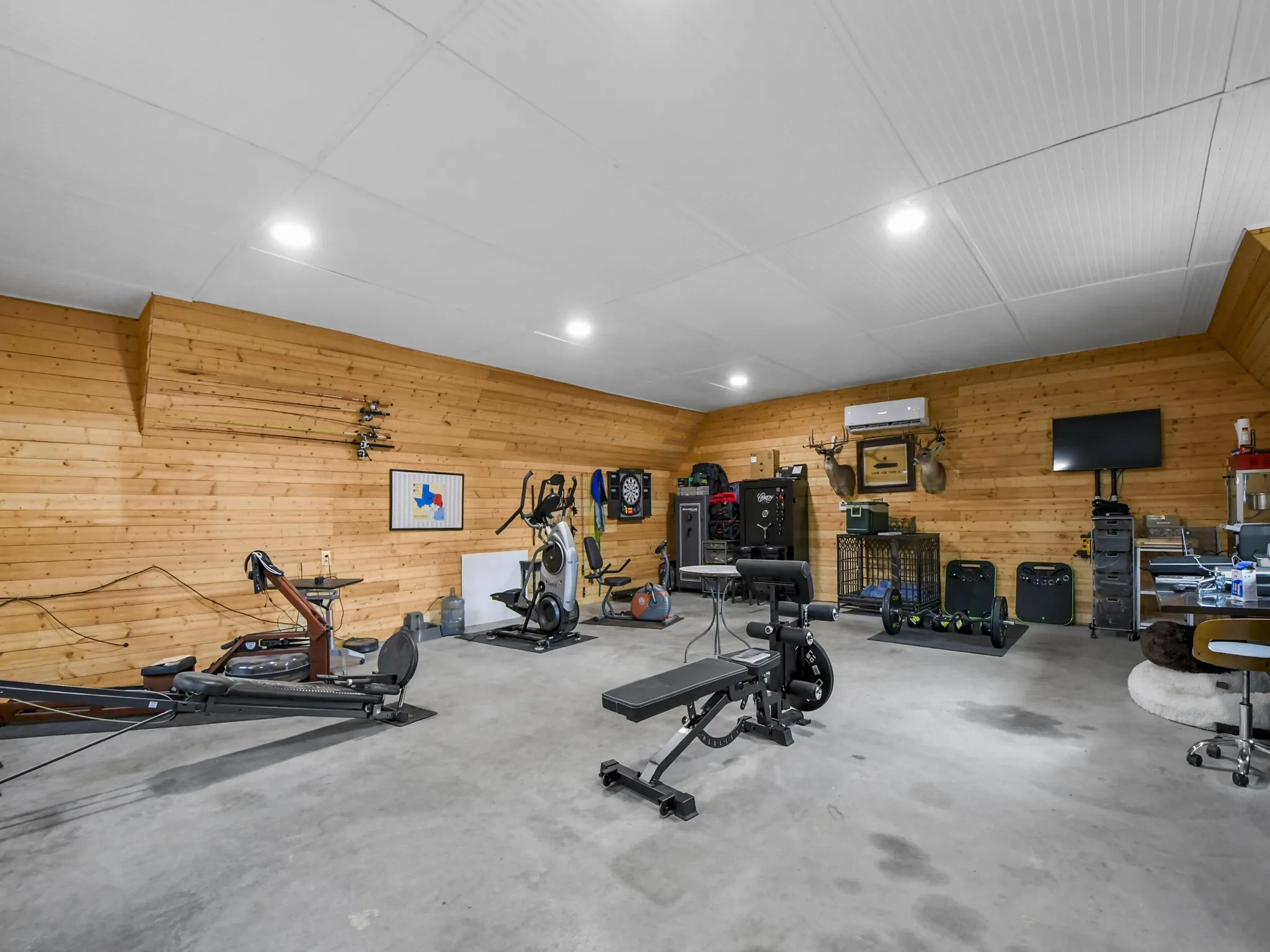 Spacious room featuring wood plank wall paneling, a concrete floor, and a white paneled ceiling with recessed lighting