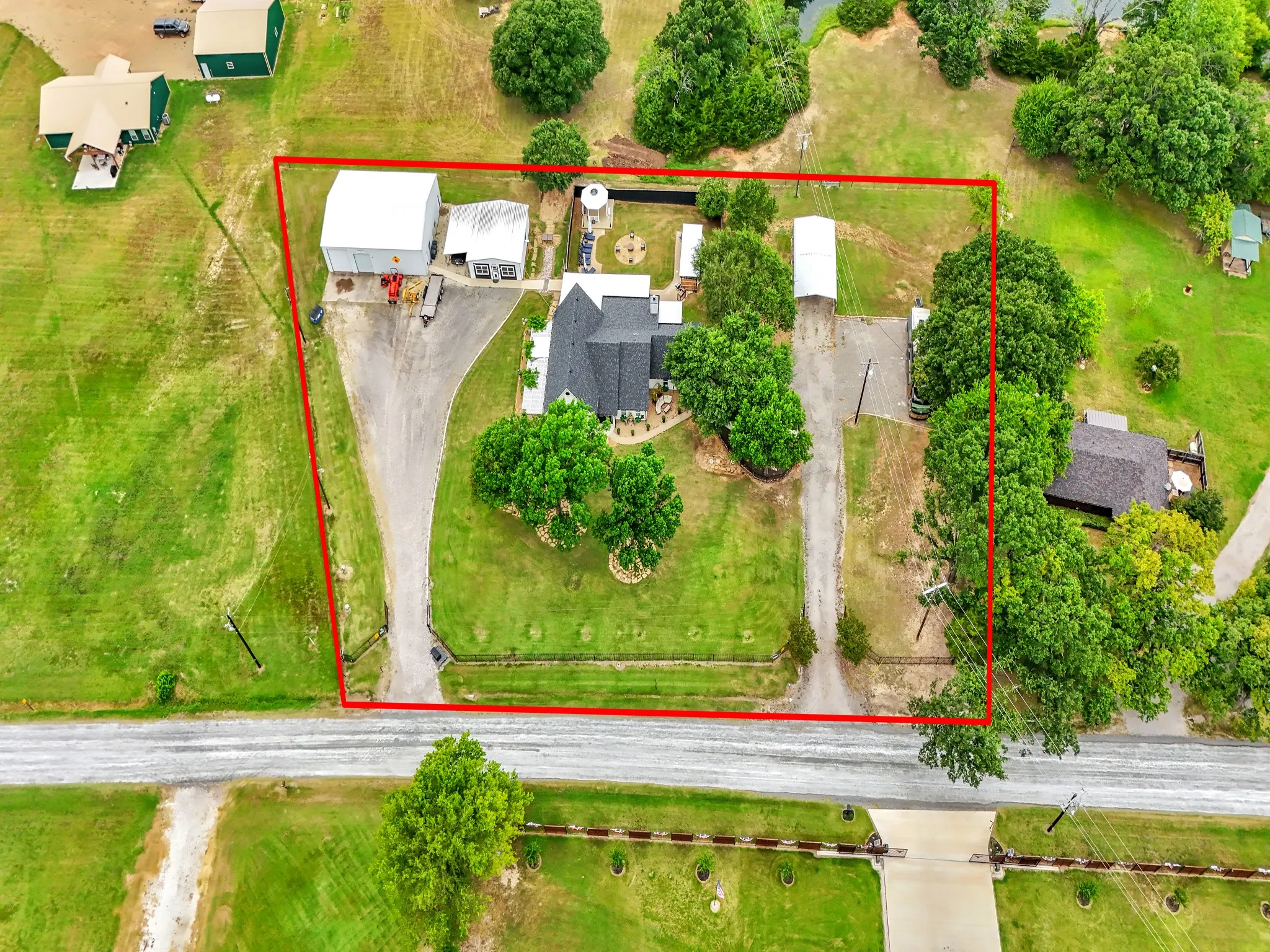 Expansive property featuring a main residence, two large outbuildings, a covered carport, and multiple mature trees