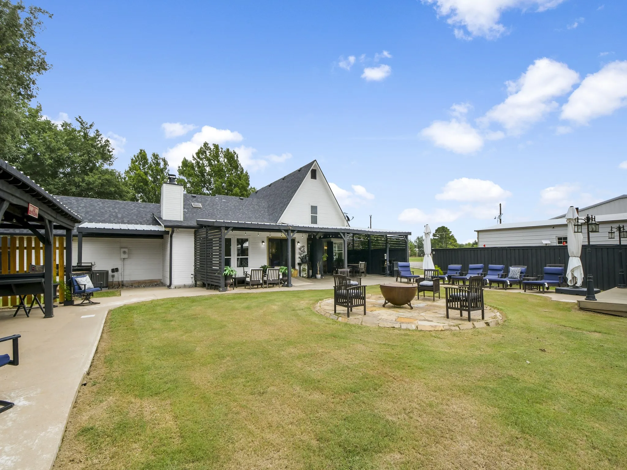 Expansive green lawn featuring a central flagstone fire pit area and a concrete pathway