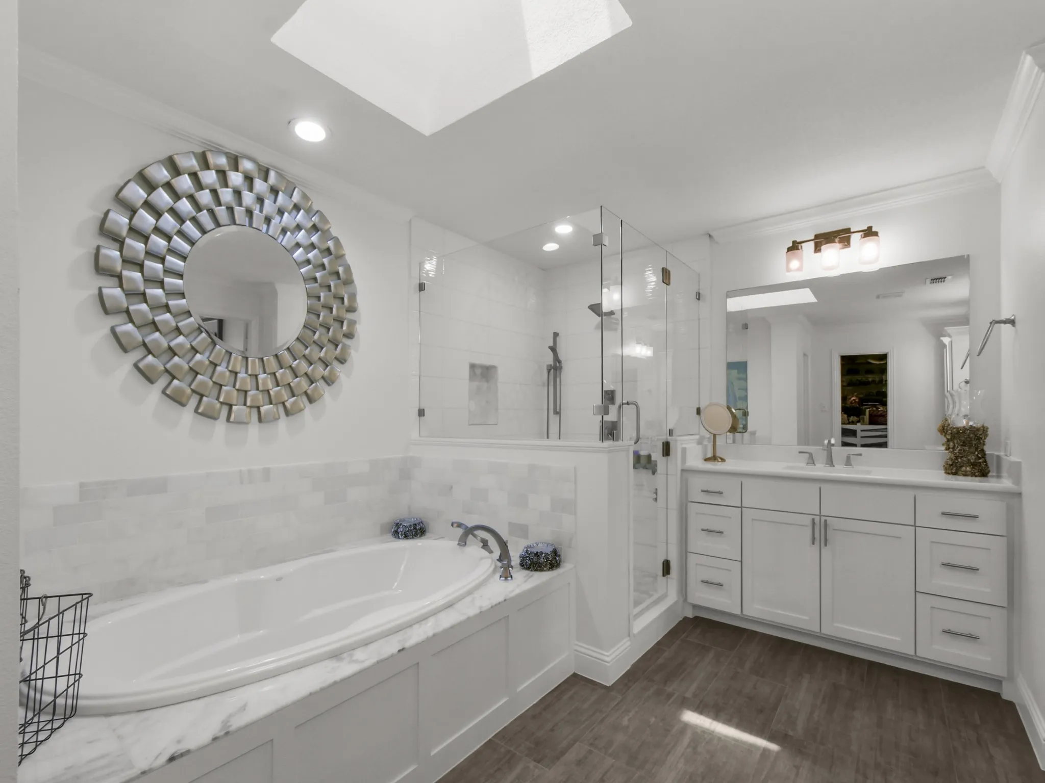 Bathroom featuring a deep soaking tub with a stone surround, a frameless glass shower enclosure, a dual-sink vanity with white cabinetry, and wood-finish flooring