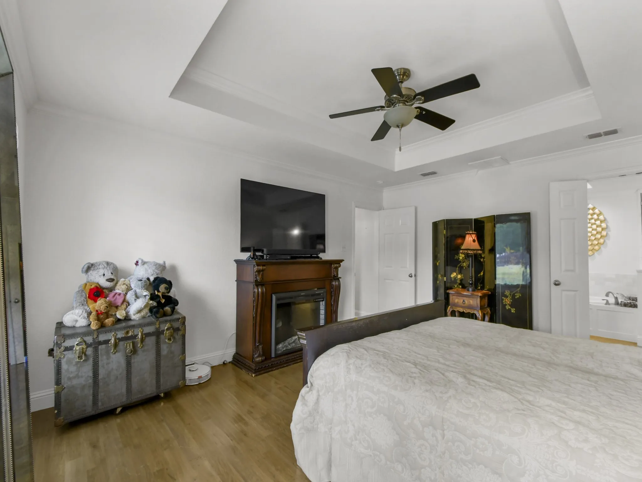 Recessed ceiling with crown molding, wood-finish flooring, and a decorative fireplace with a mantel