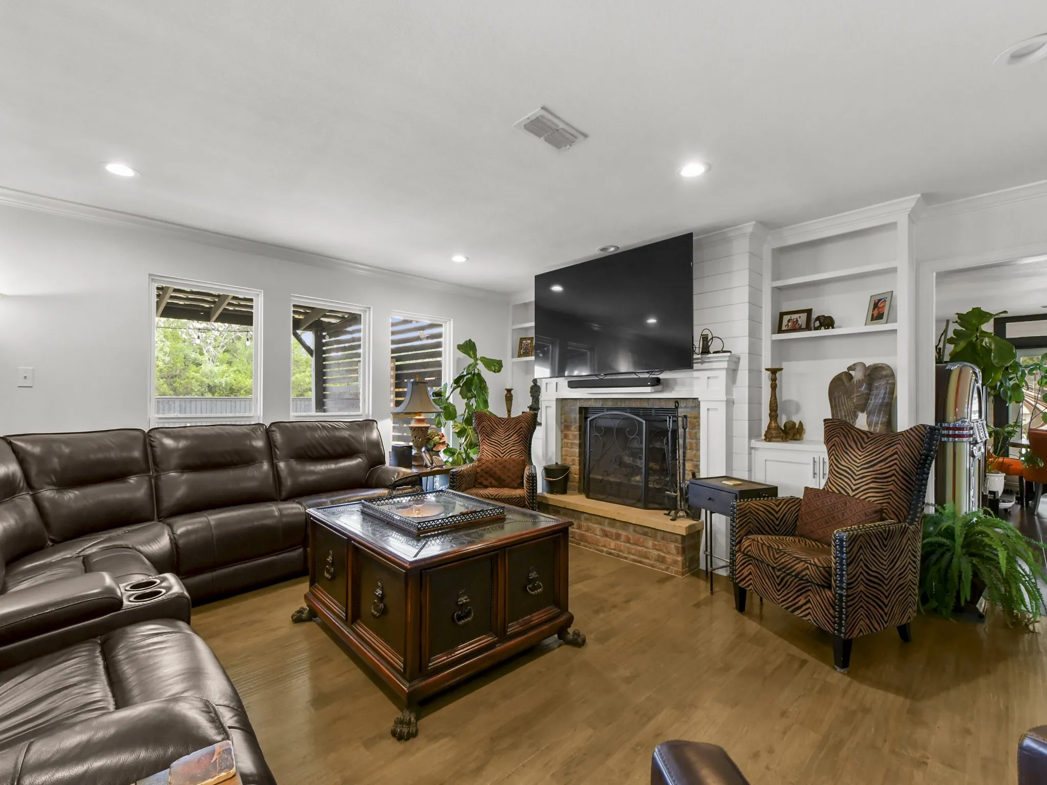 Living area featuring wood-finish flooring, a brick fireplace with a white mantel, built-in shelving, recessed lighting, and multiple windows
