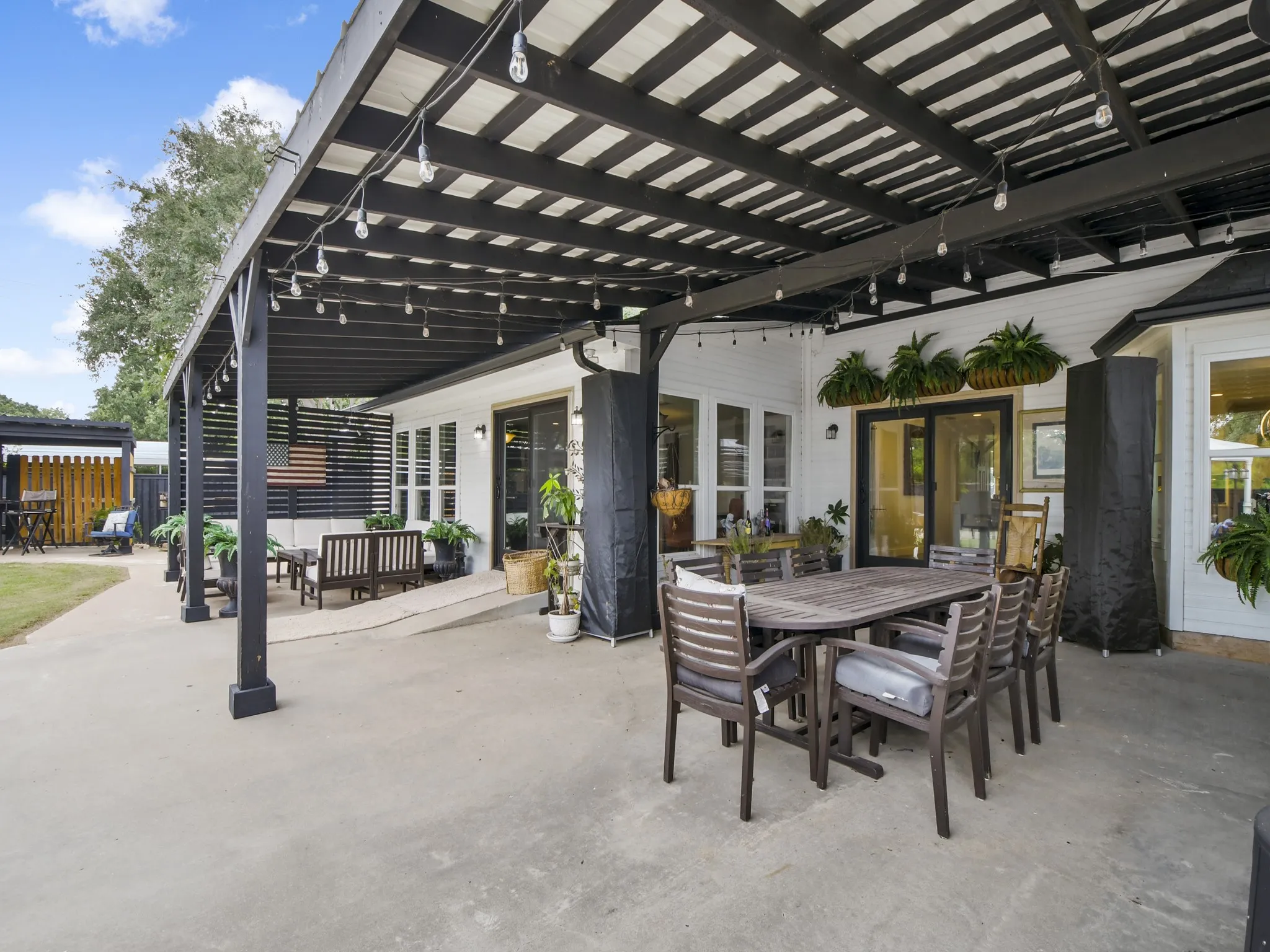 Expansive concrete patio area with a black wood pergola, white exterior siding, and multiple glass doors