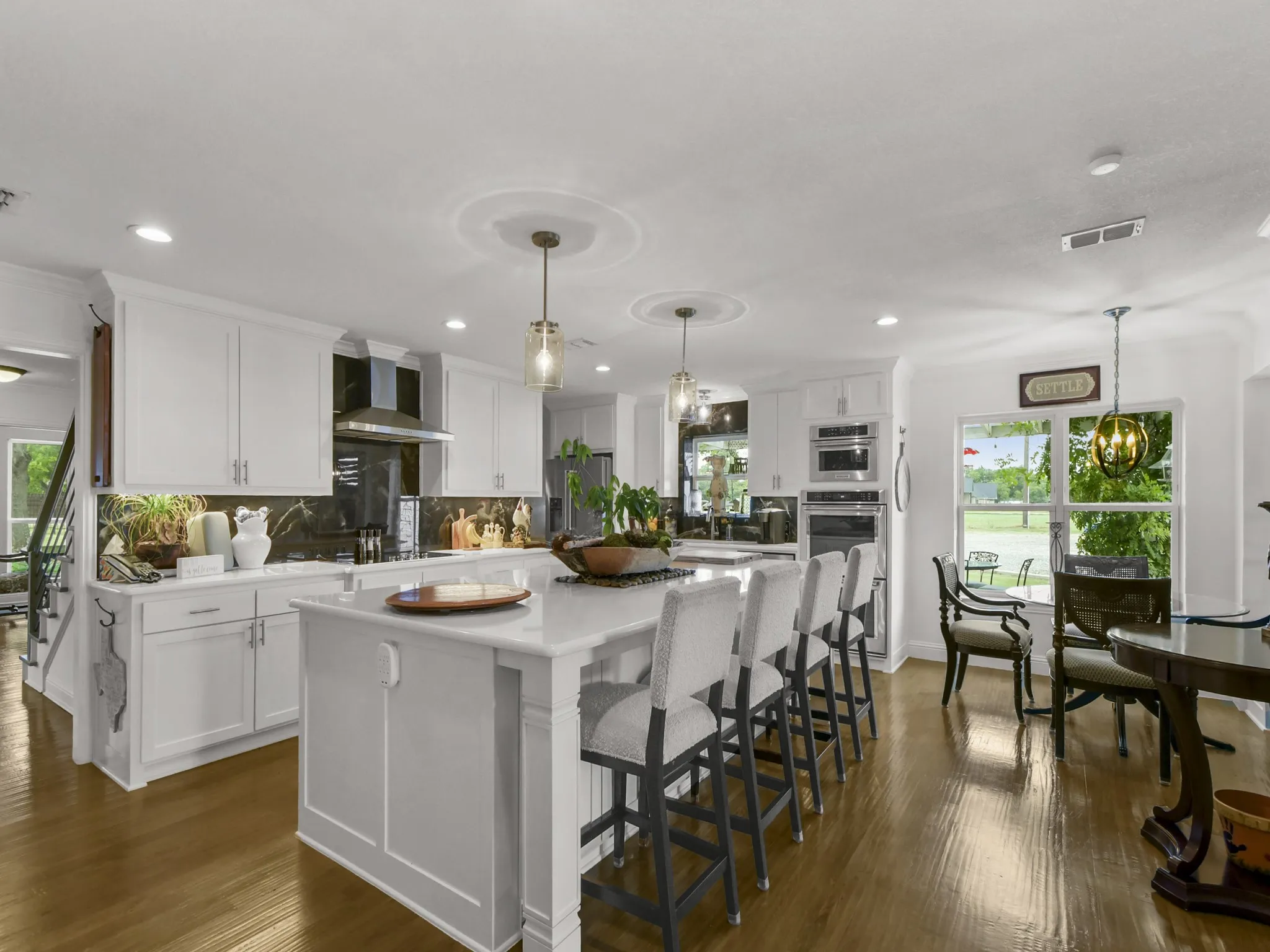 Spacious kitchen with a central island featuring a white countertop and seating, complemented by white cabinetry and dark stone slab backsplash