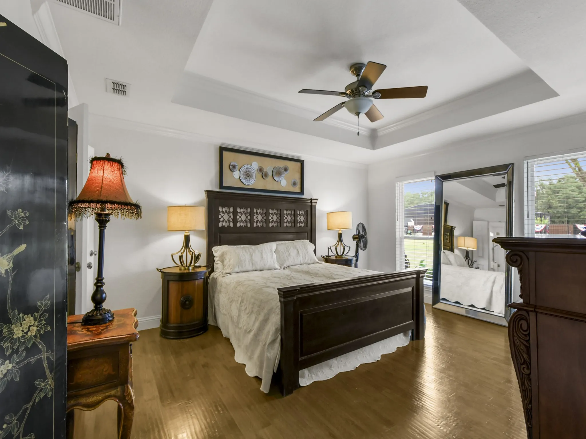 Bedroom with tray ceiling and crown molding, featuring wood-finish flooring, a ceiling fan, and large windows with blinds