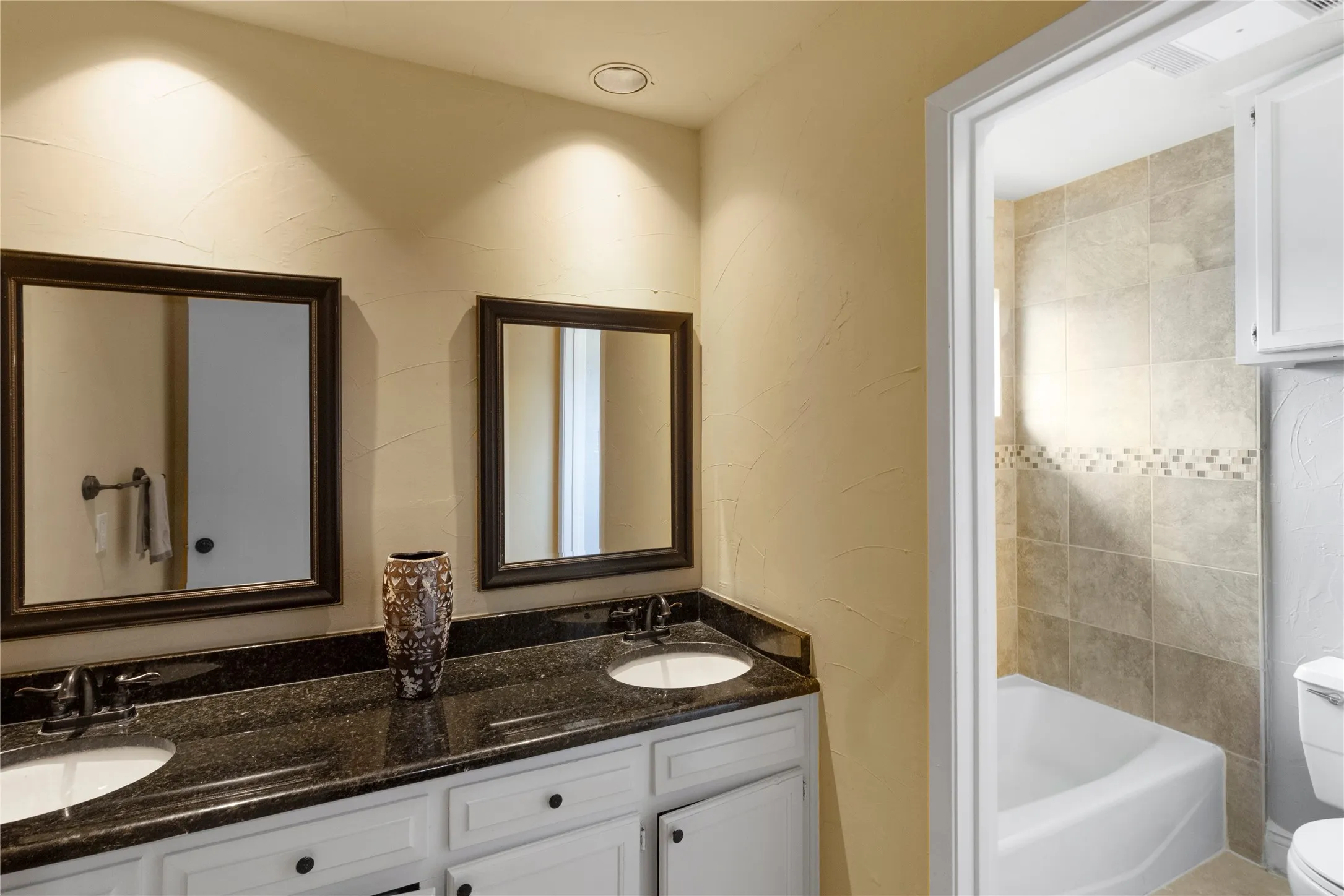 Dual vanity with dark stone countertop, white cabinetry, and framed mirrors