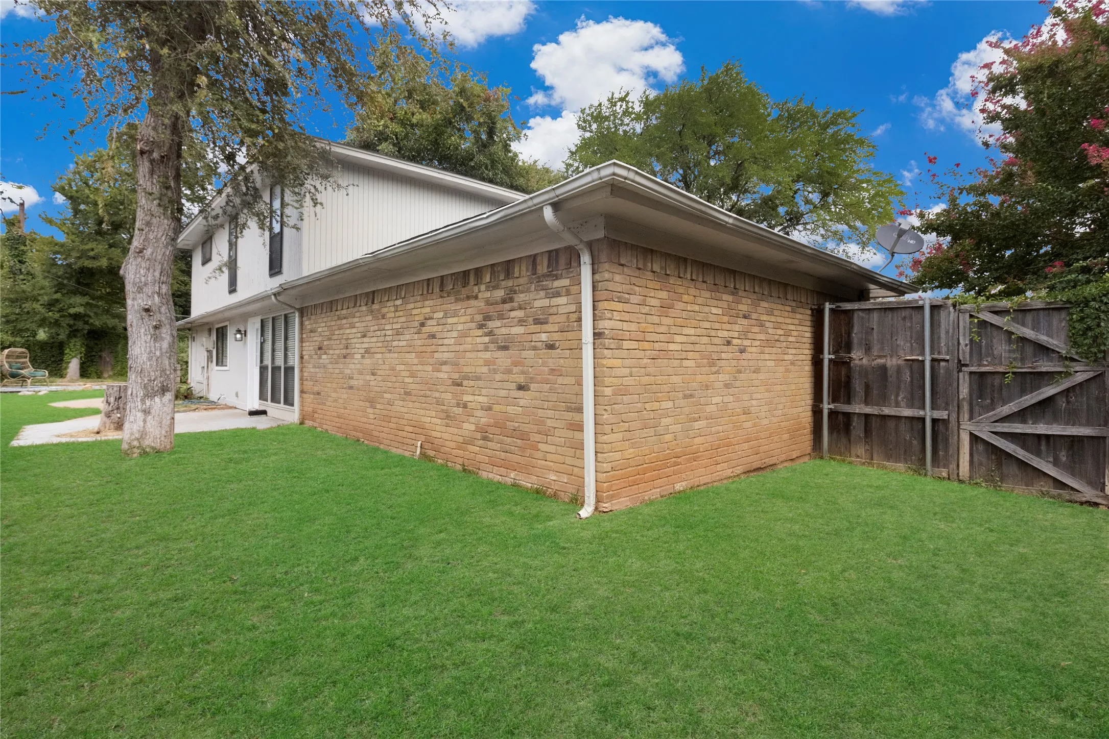 Brick exterior with white siding, wood privacy fence, concrete patio, and a mature tree