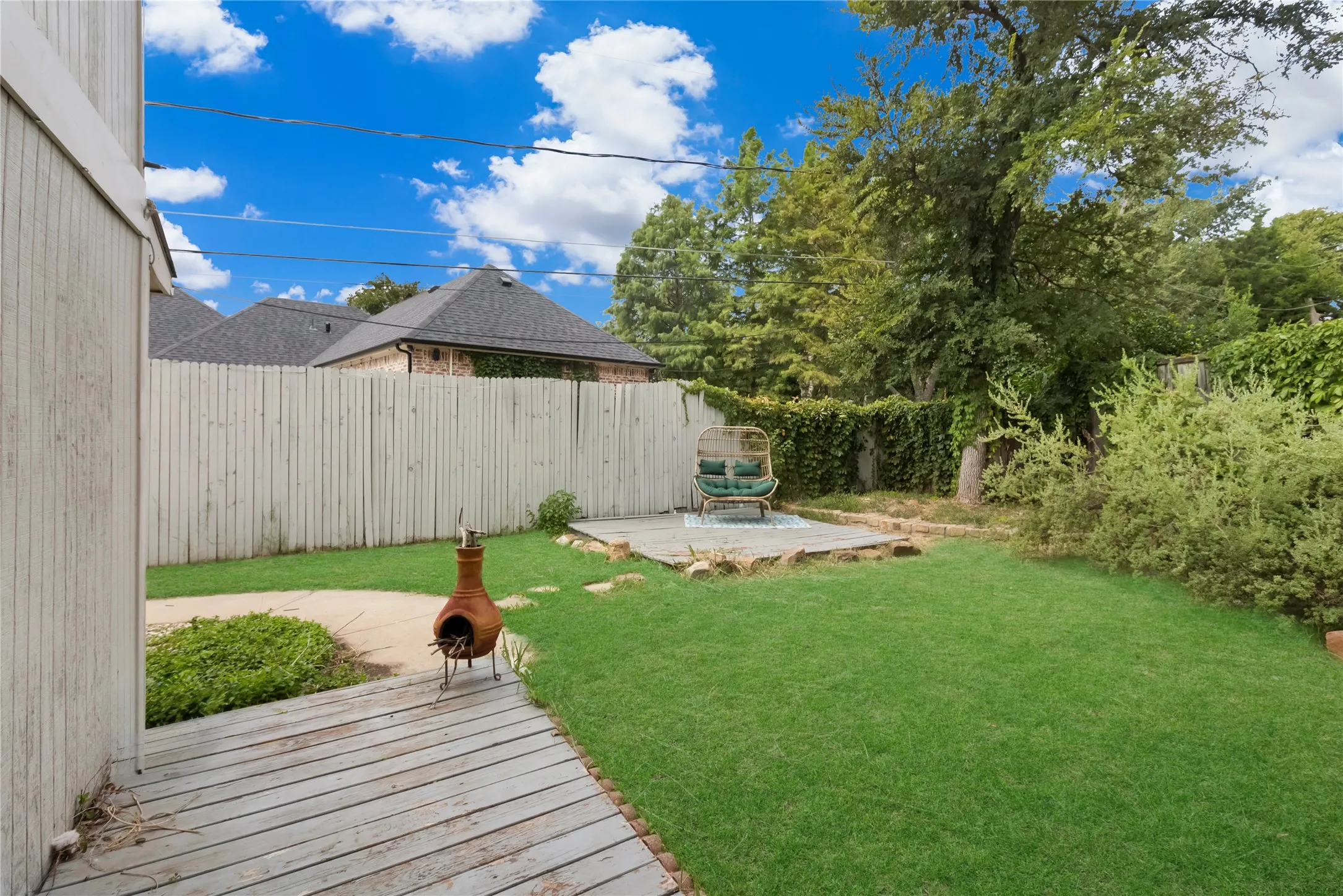 Fenced backyard featuring a wood-finish deck, manicured lawn, and a stone-paved patio