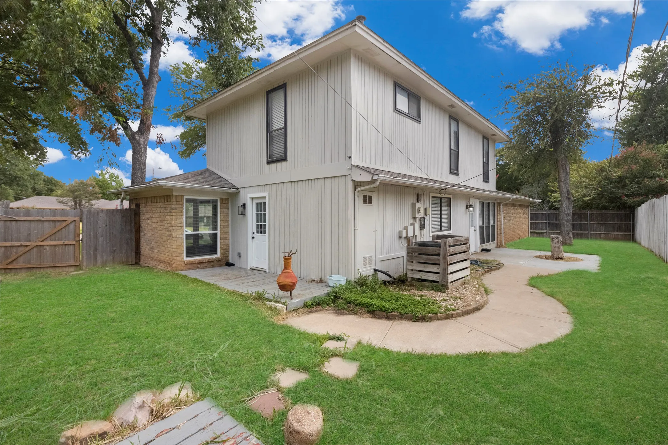 Expansive yard featuring a concrete patio, mature trees, and a wooden privacy fence