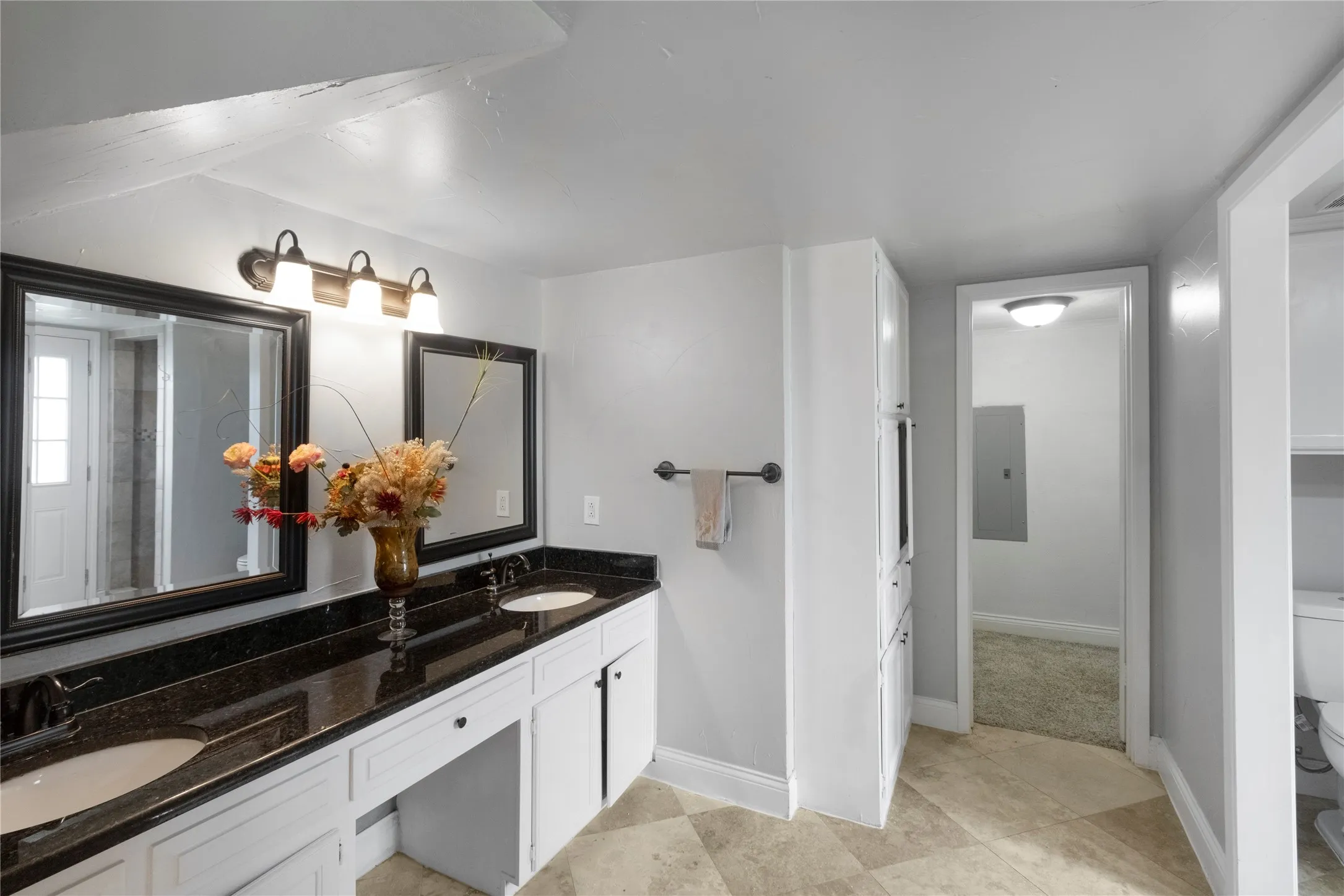 Spa-inspired primary bathroom featuring dual vanities with black stone countertops, polished chrome fixtures, and framed mirrors with integrated lighting