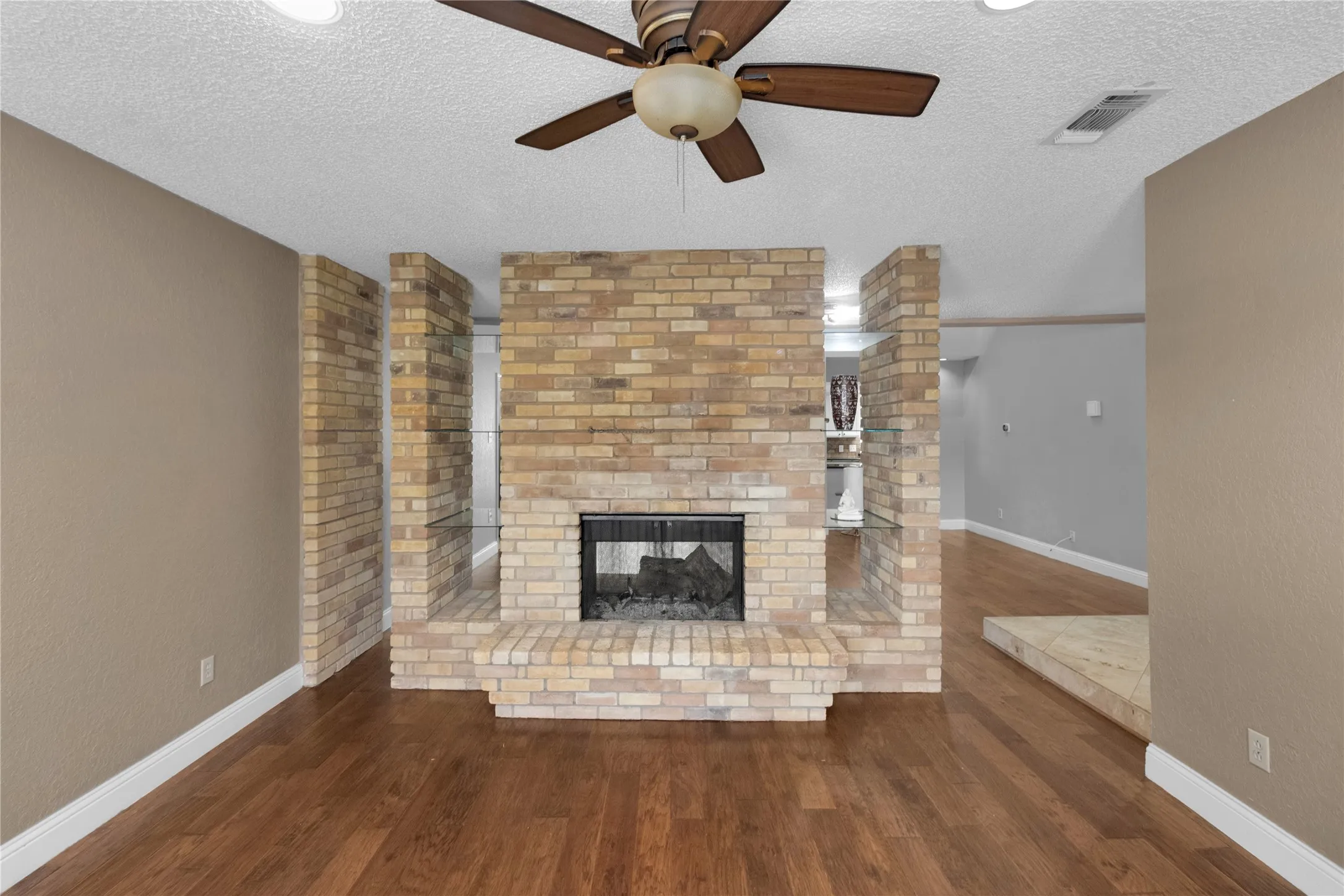 Brick fireplace with a raised hearth, wood-finish flooring, and a ceiling fan