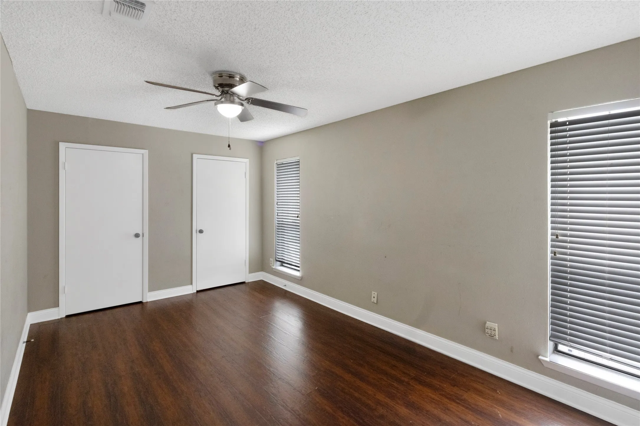 Wood-finish flooring, two windows with blinds, ceiling fan with integrated lighting, and two white doors