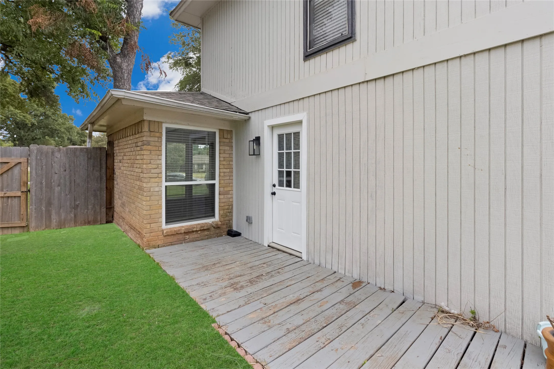 Brick-clad extension with a single window, white paneled exterior, wood deck, and a white entry door with glass panels