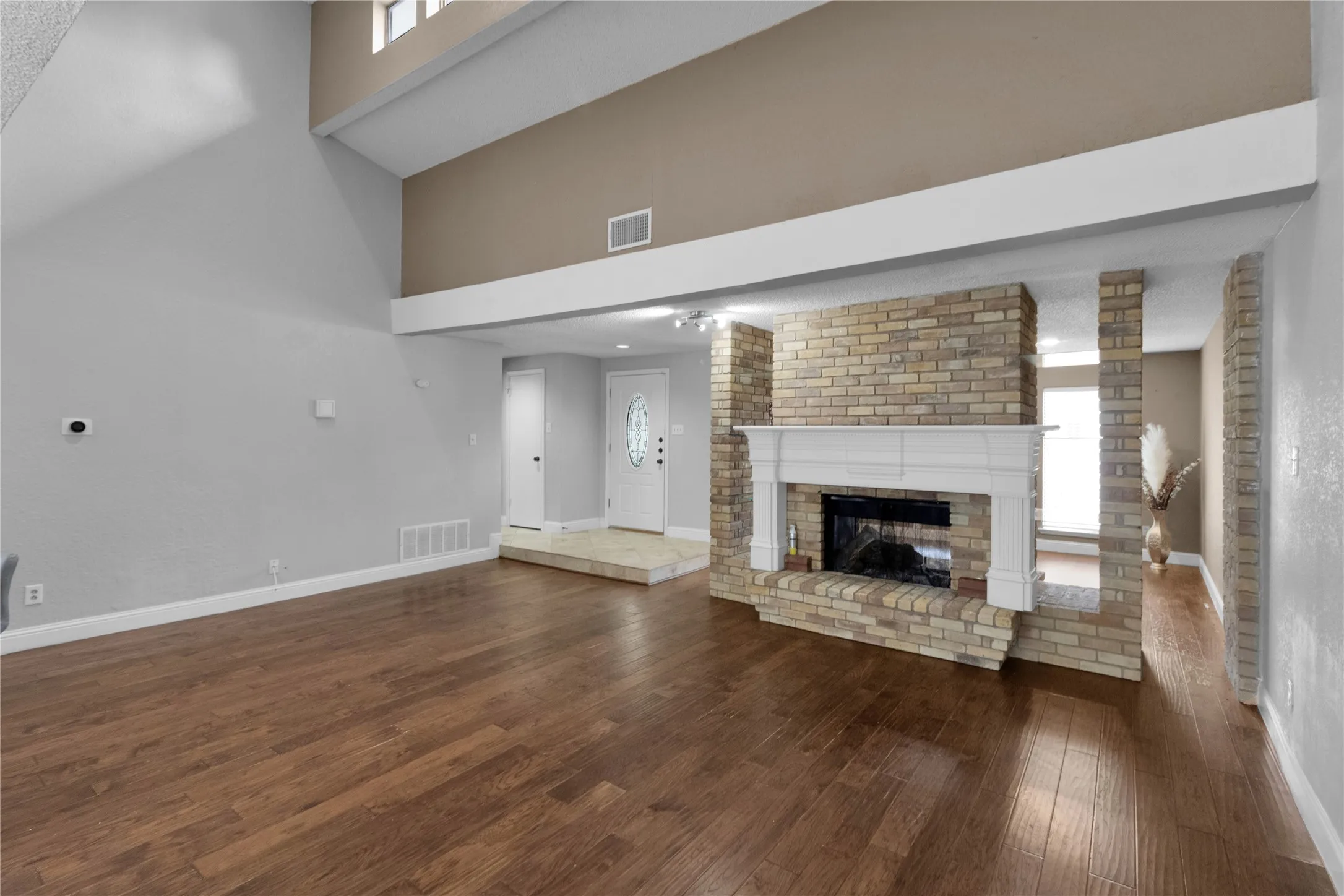 Spacious room featuring wood-finish flooring, a brick fireplace with a white mantel, and a vaulted ceiling