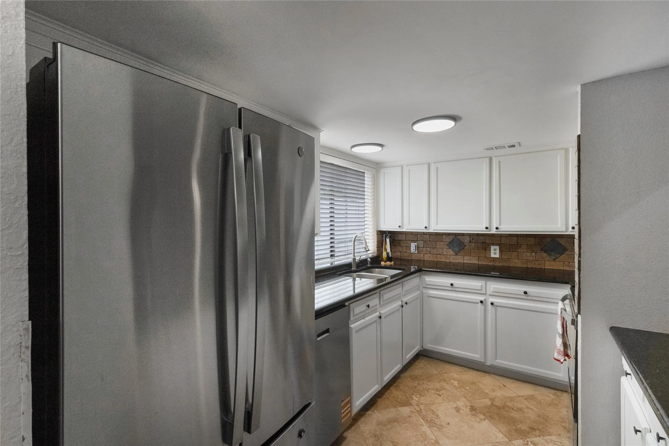 Stainless steel refrigerator, white cabinetry, dark countertops, tile backsplash, and light-colored flooring