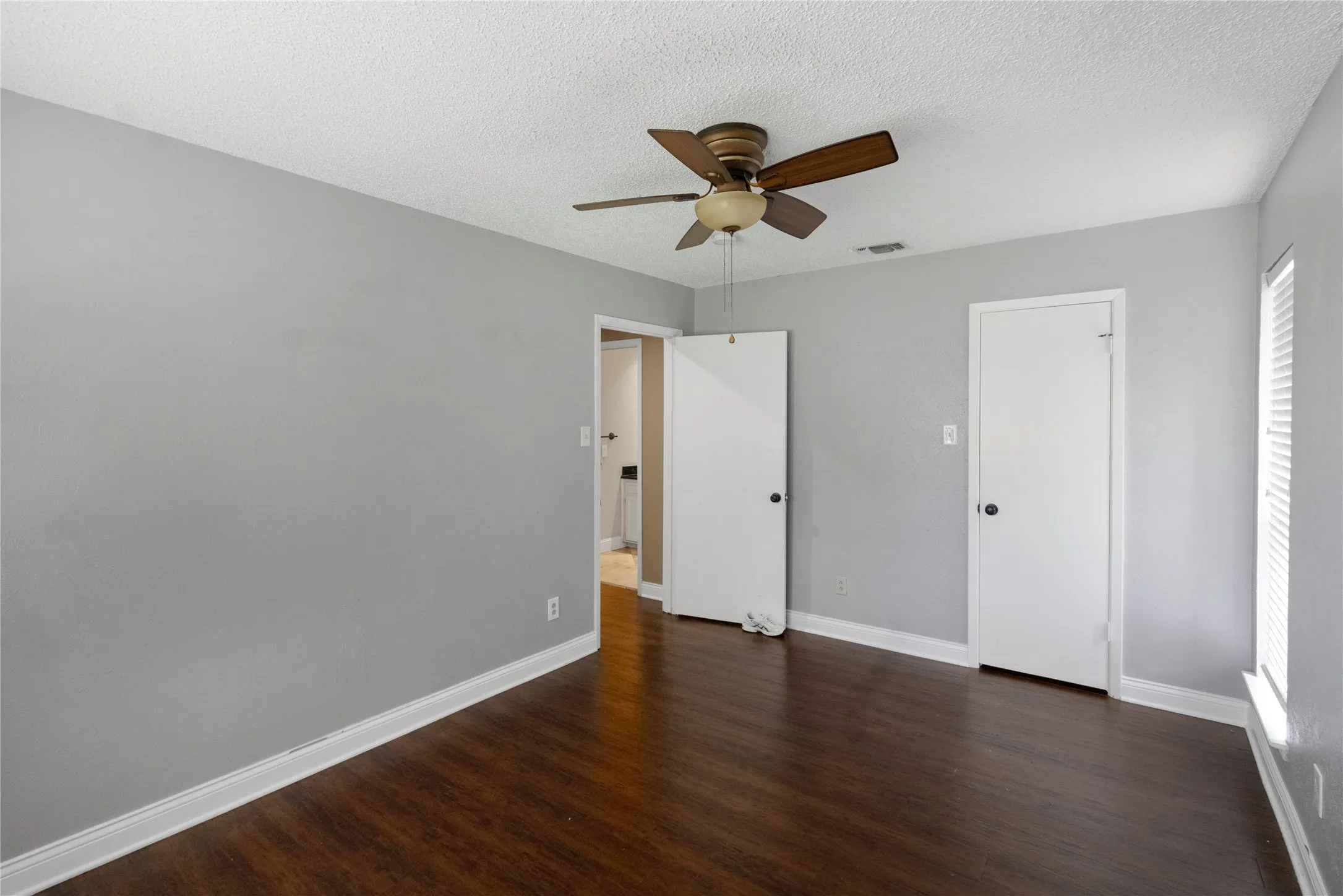 Wood-finish flooring, ceiling fan with integrated lighting, window with blinds, and painted walls