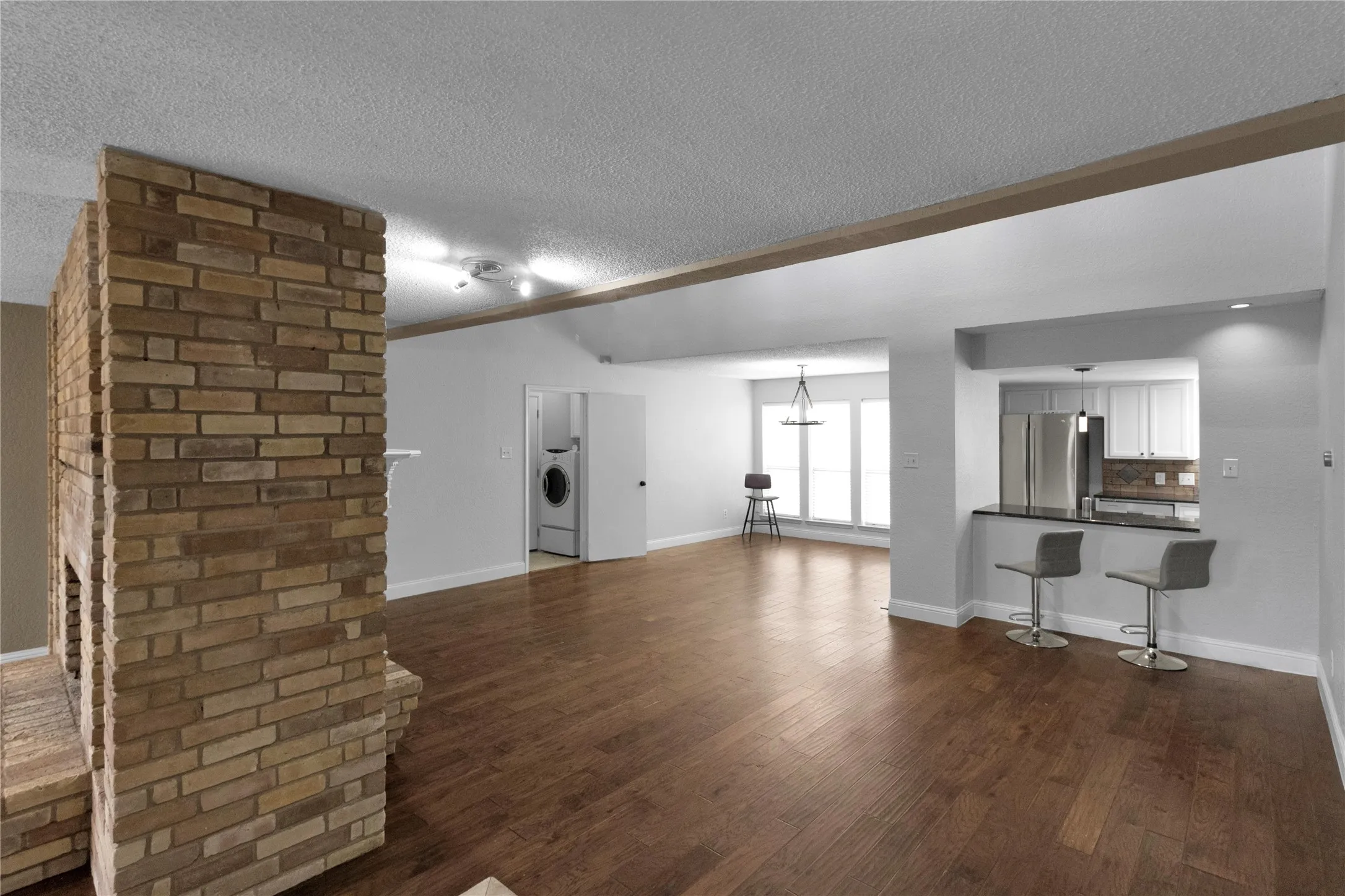 Brick fireplace with hearth, wood-finish flooring, recessed lighting, kitchen pass-through with counter, and stainless steel appliances