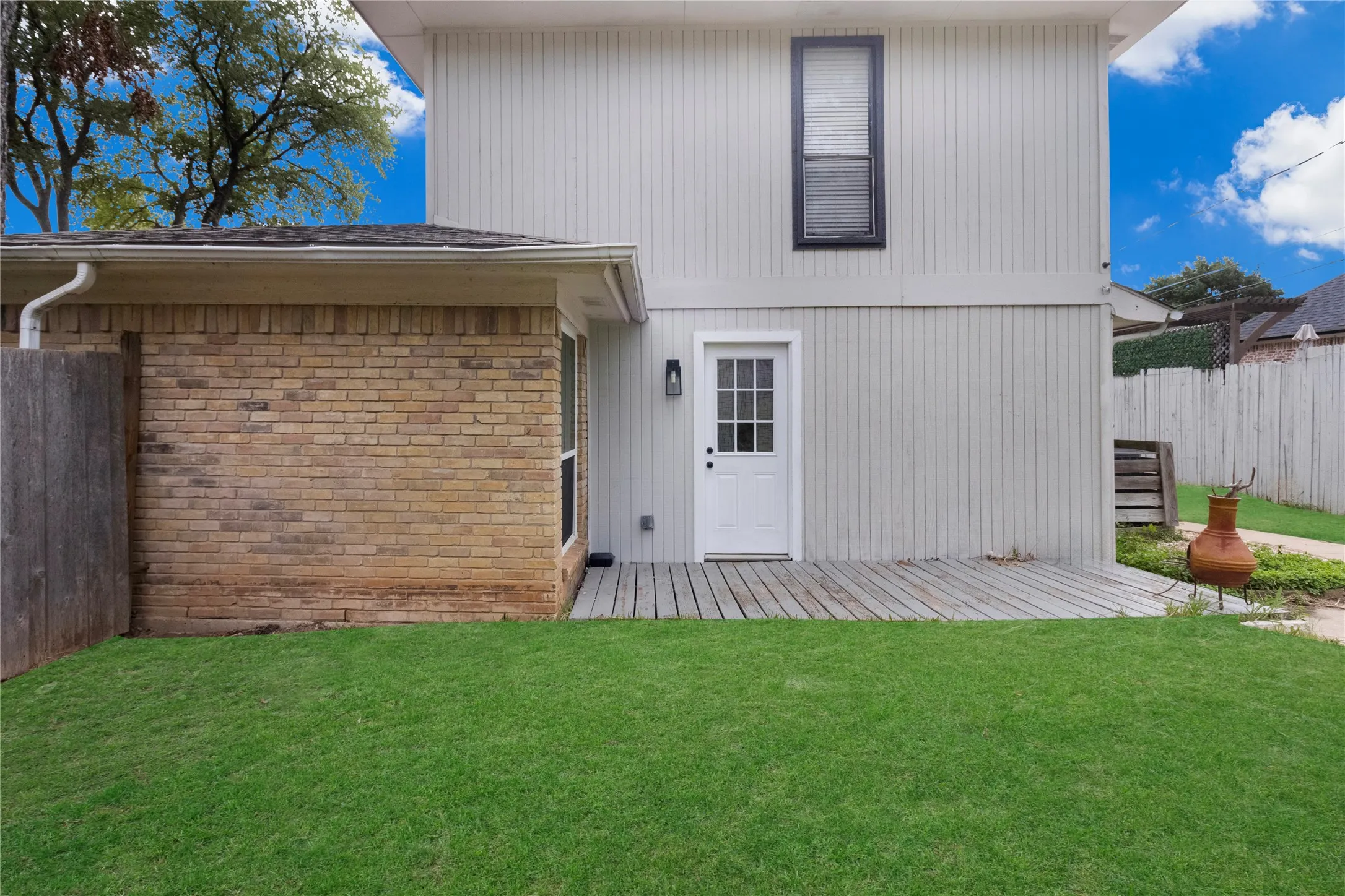 Expansive backyard featuring a manicured lawn, wood deck, and a white paneled door with an exterior light fixture