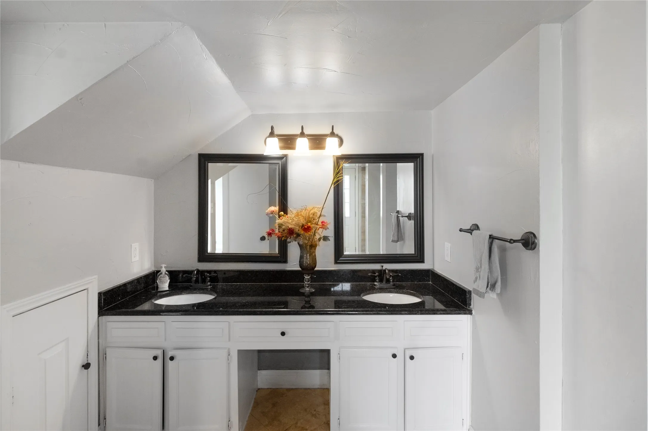 Dual sink vanity with black countertops, white cabinetry, and framed mirrors