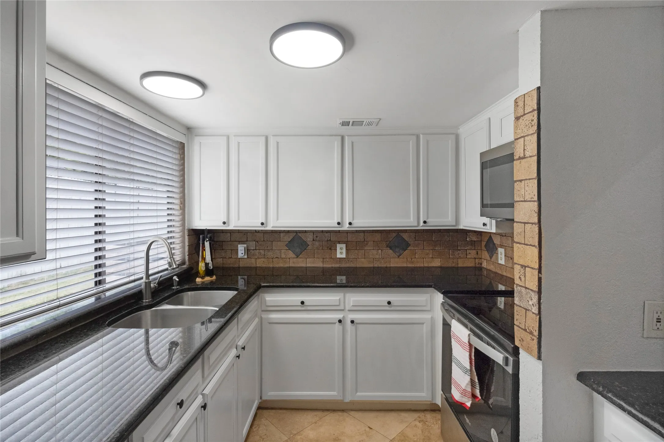 U-shaped kitchen featuring white cabinetry, dark countertops, a double basin stainless steel sink with a gooseneck faucet, and a tile backsplash