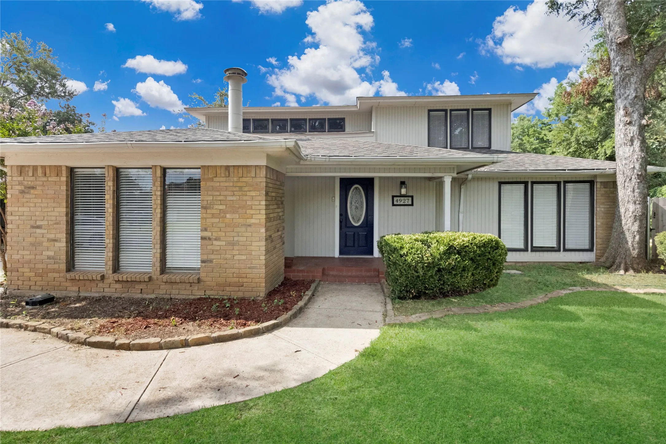 Exterior featuring brick and siding finishes, multi-pane windows, a dark paneled front door, and a manicured lawn