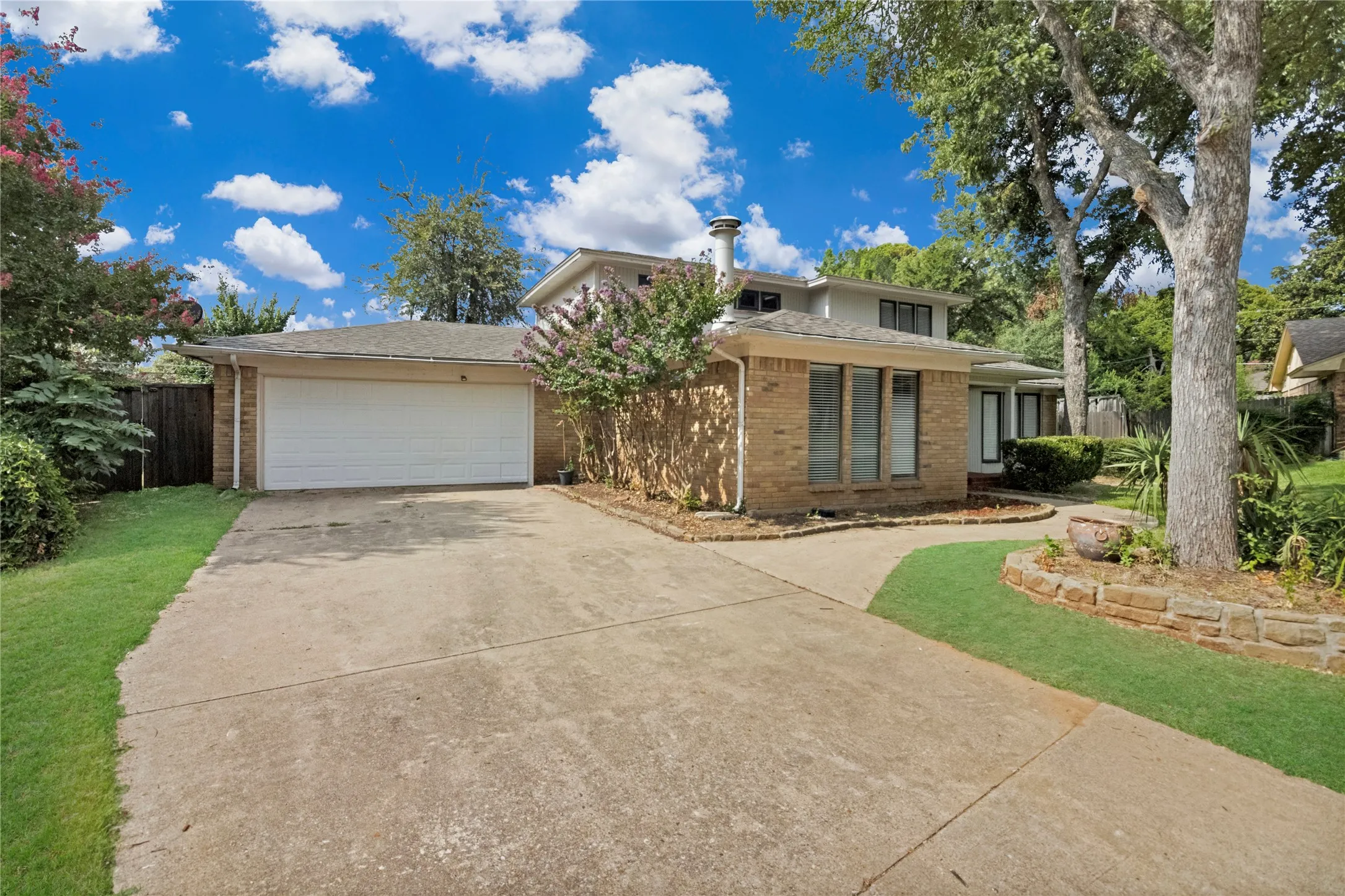 Brick exterior with an integrated two-car garage, concrete driveway, and mature landscaping