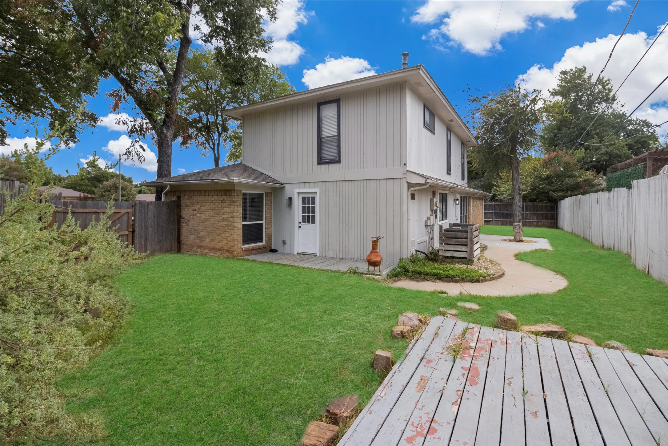 Expansive backyard featuring a concrete patio, a wood deck, a mature tree, and a brick and siding exterior