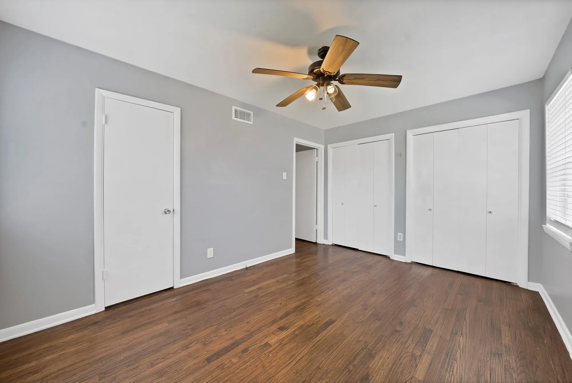 Bedroom featuring wood-finish flooring, light gray walls, a ceiling fan with integrated lighting, two bi-fold door closets, and a window with blinds